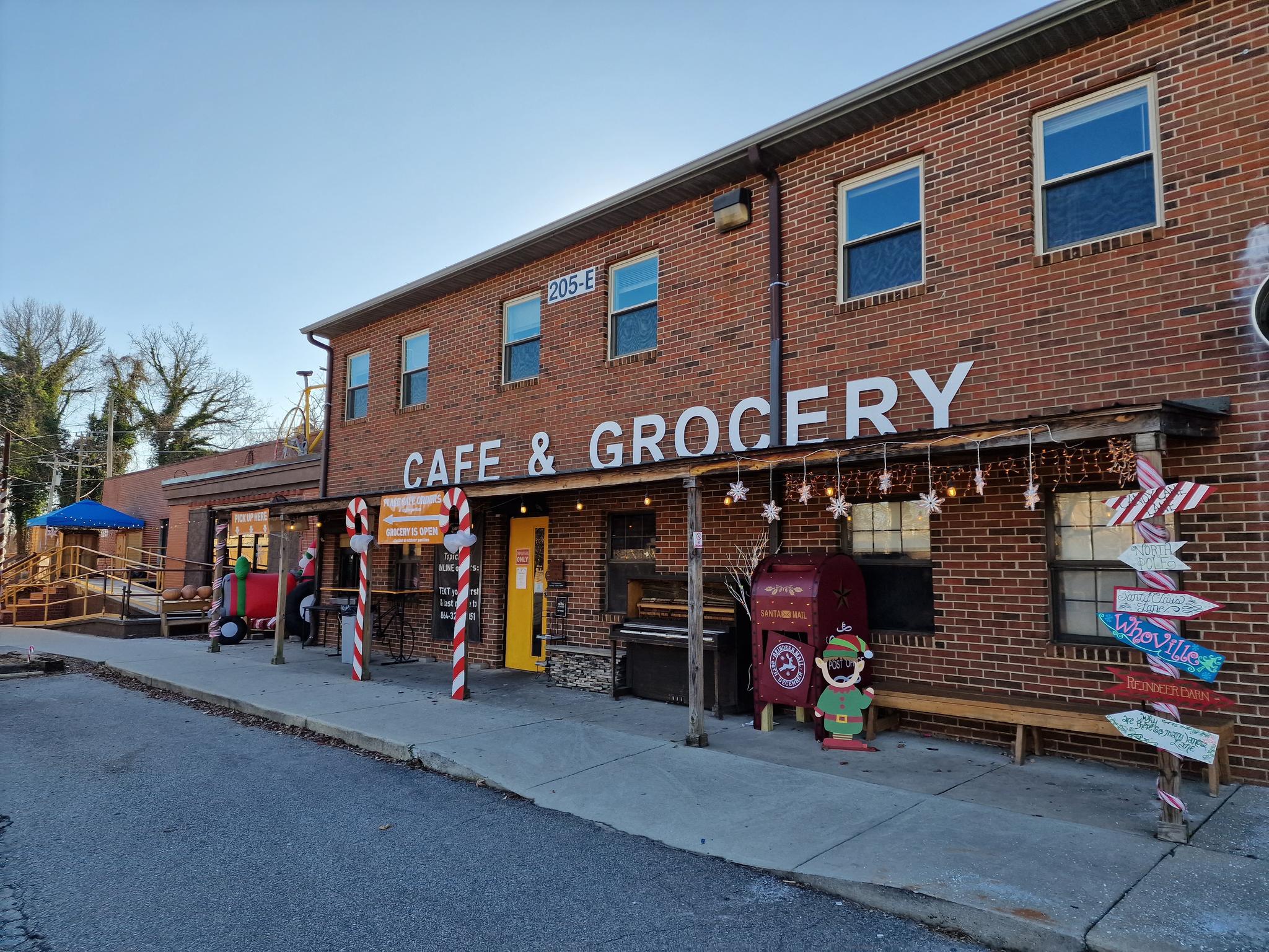 A brick cafe and grocery store with festive decorations on a sunny day.