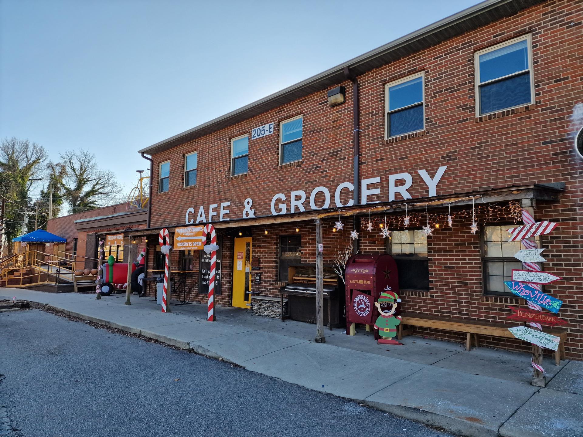 A brick cafe and grocery store with festive decorations on a sunny day.
