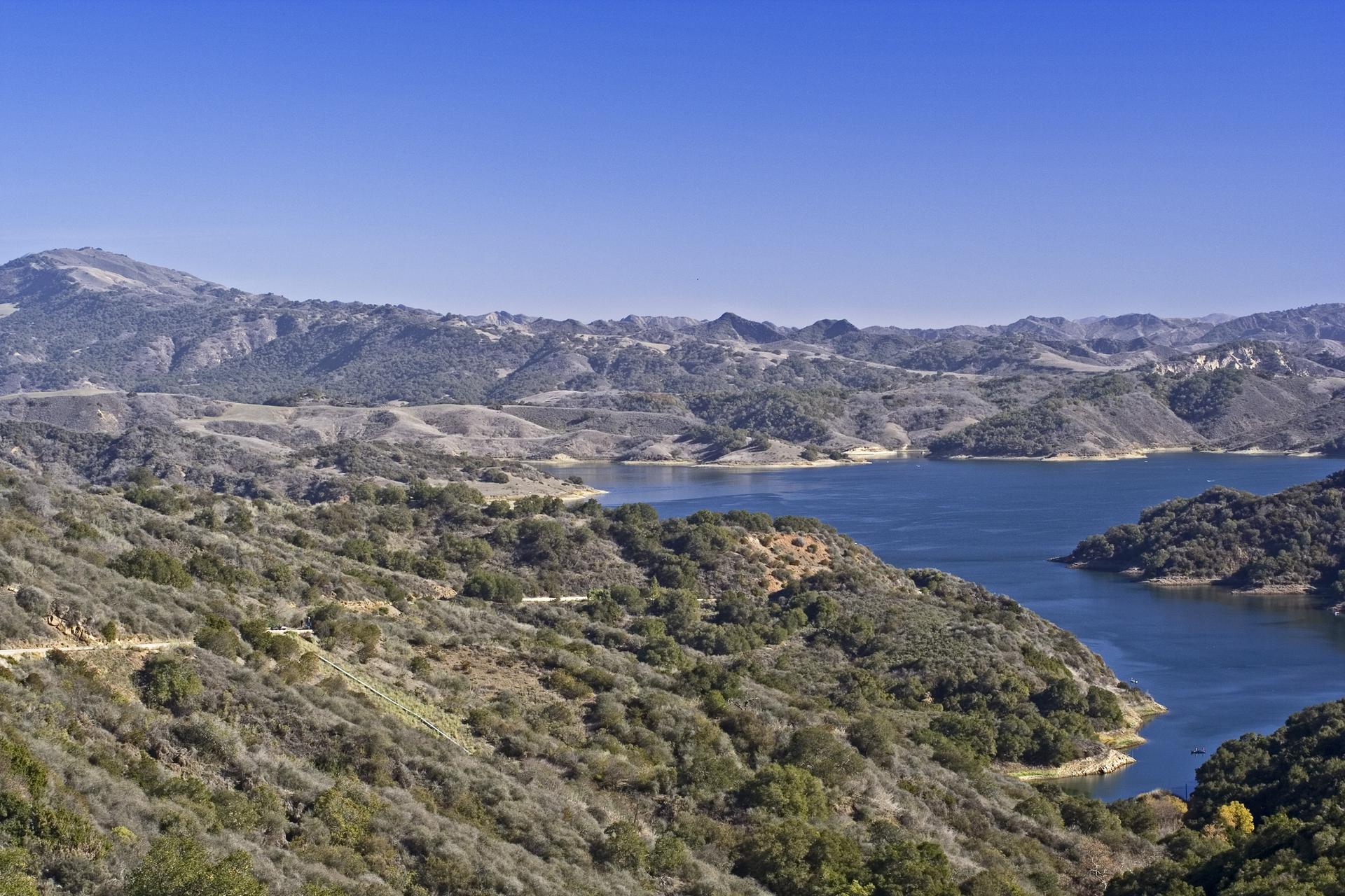 Expansive view of a blue lake surrounded by green, rugged mountains.