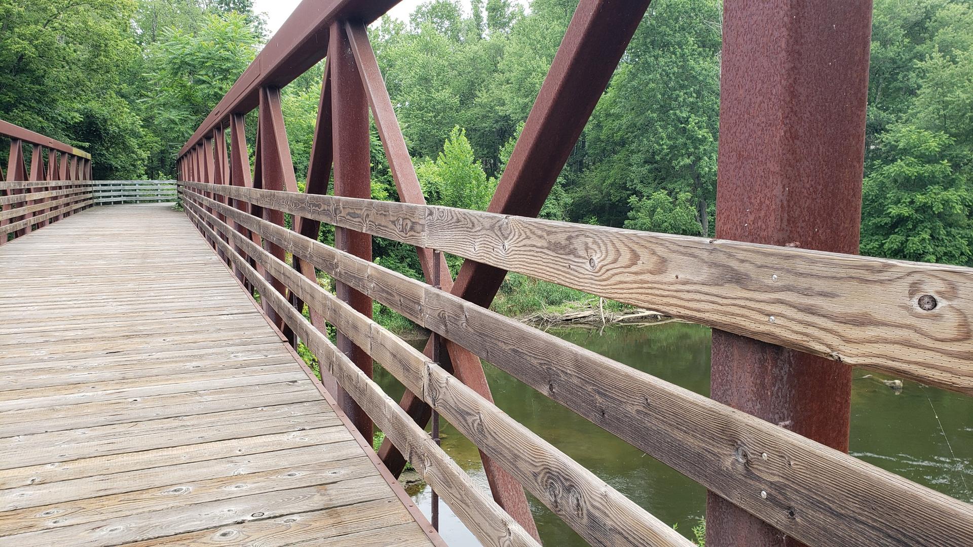 Wooden and metal bridge railing over water, surrounded by green trees.