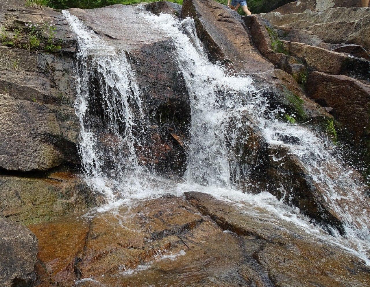 Water cascades over dark, mossy rocks, with a person's legs visible above.