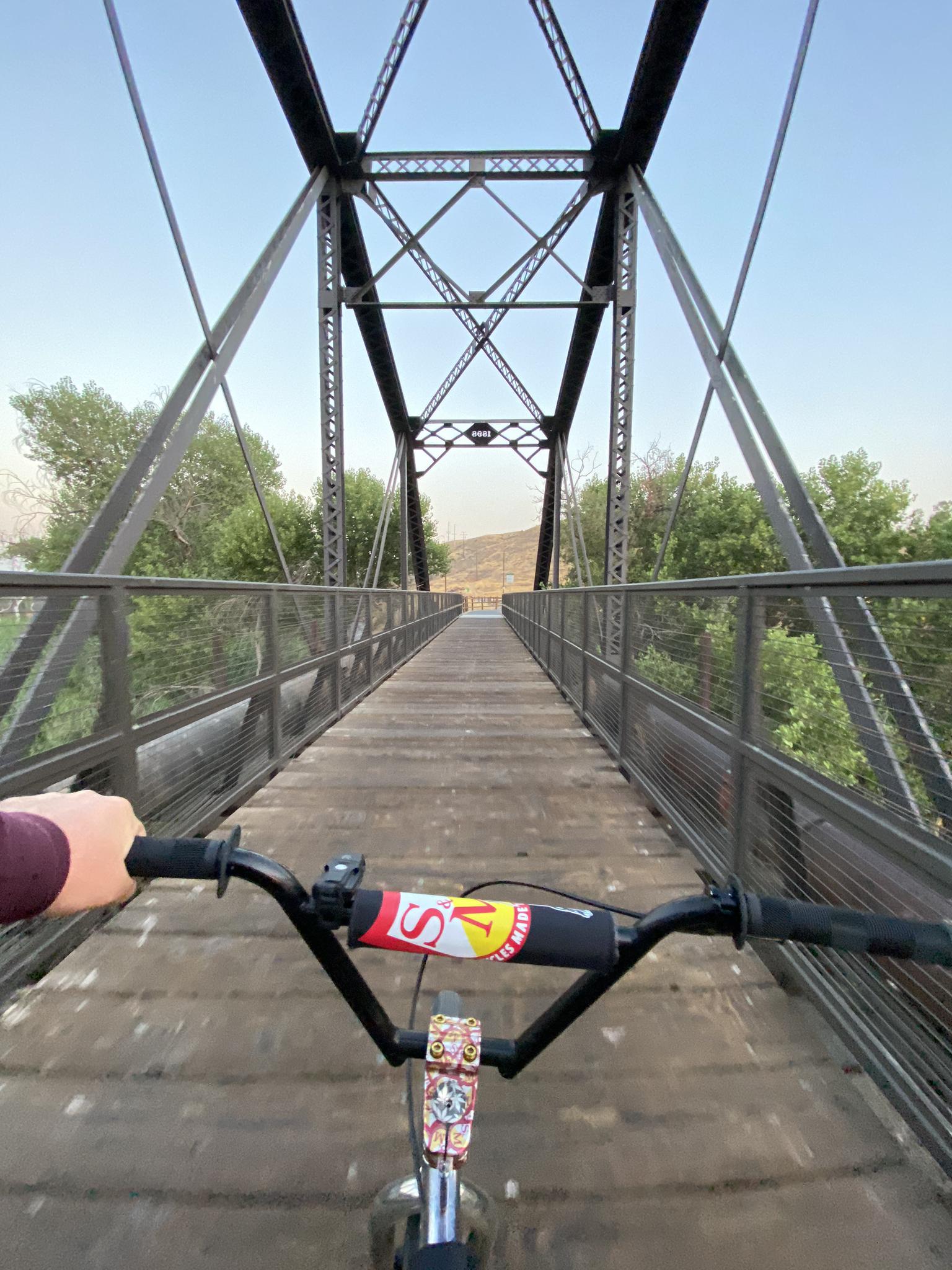 First-person view of a person cycling across a long metal truss bridge.