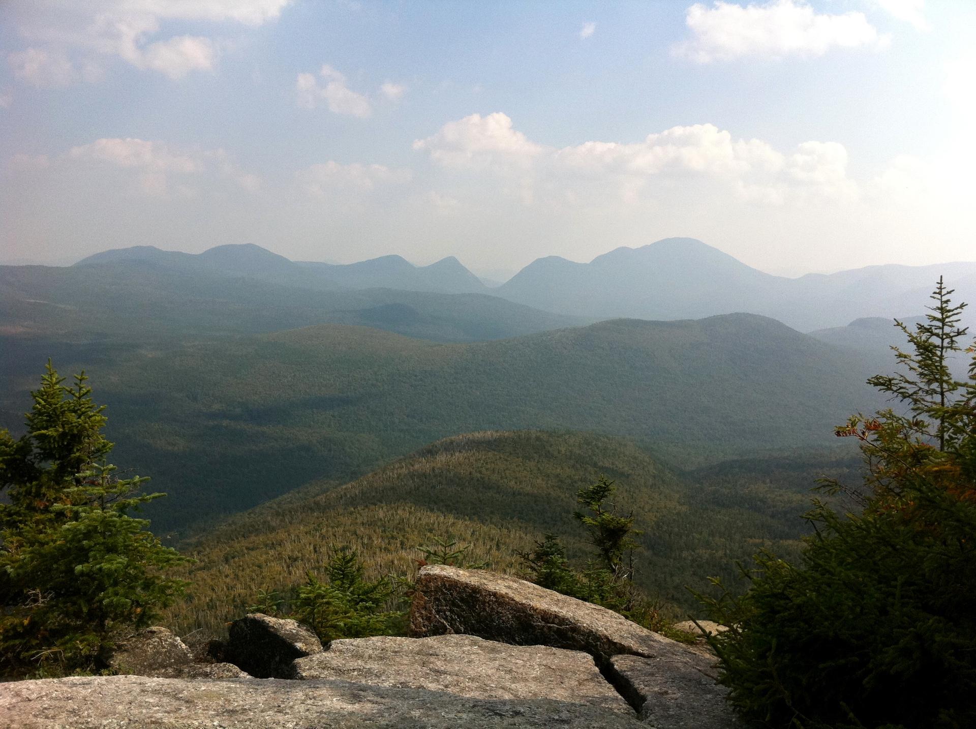 Expansive view of hazy, forested mountains under a partly cloudy sky.