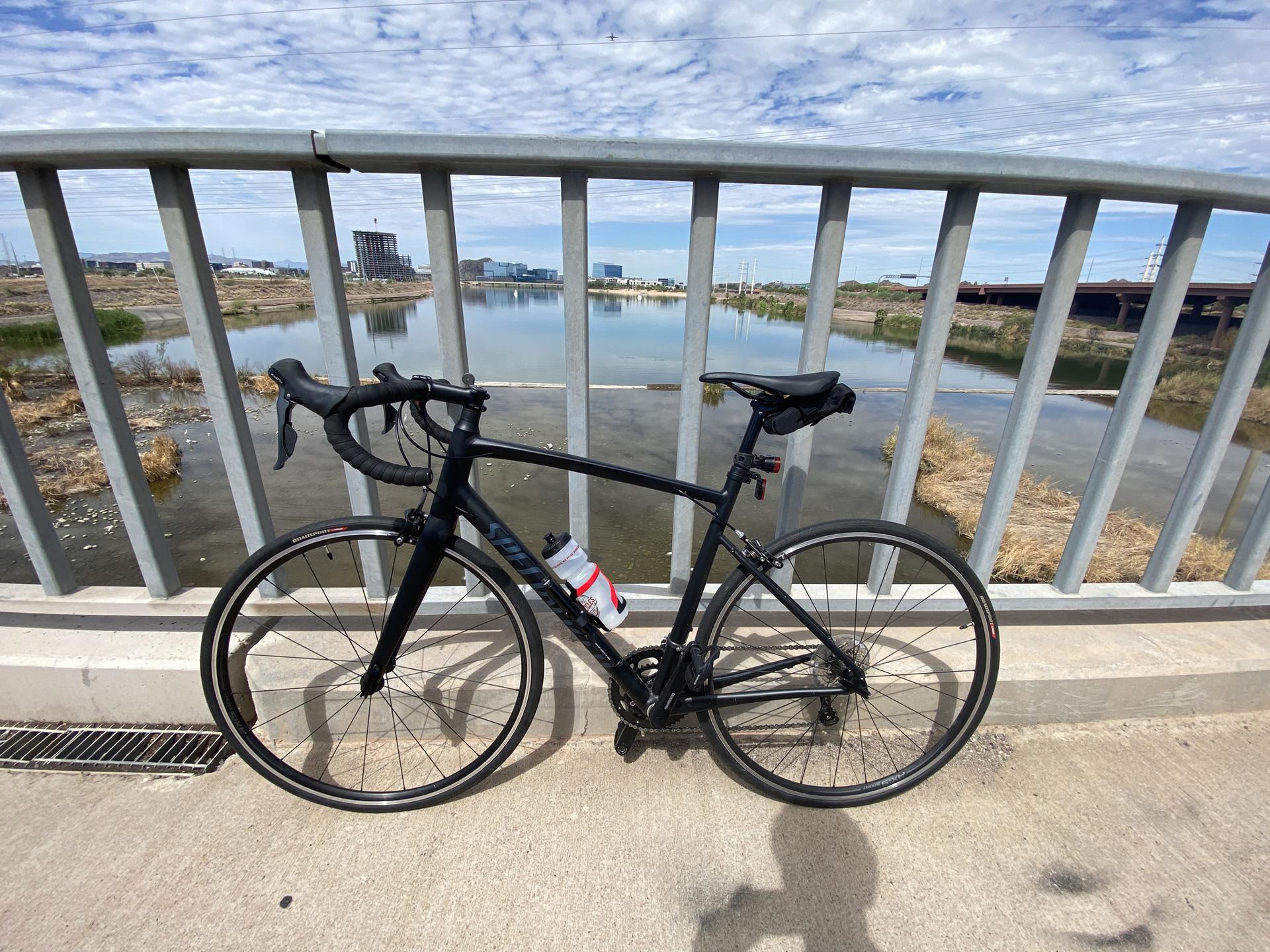 A black bicycle rests on a bridge overlooking water, cloudy sky.