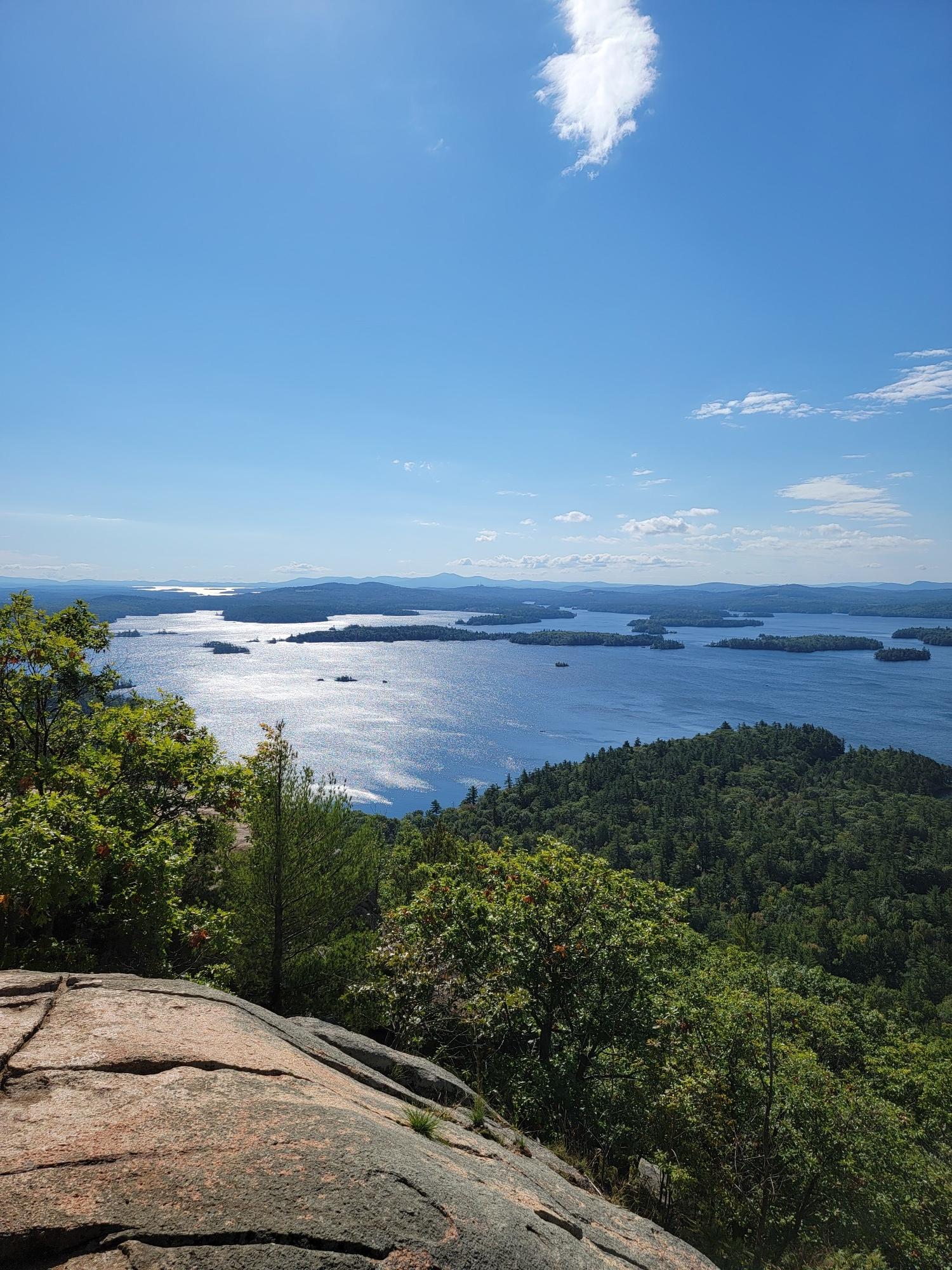 Sunny panoramic view of a large lake with islands and green forests.