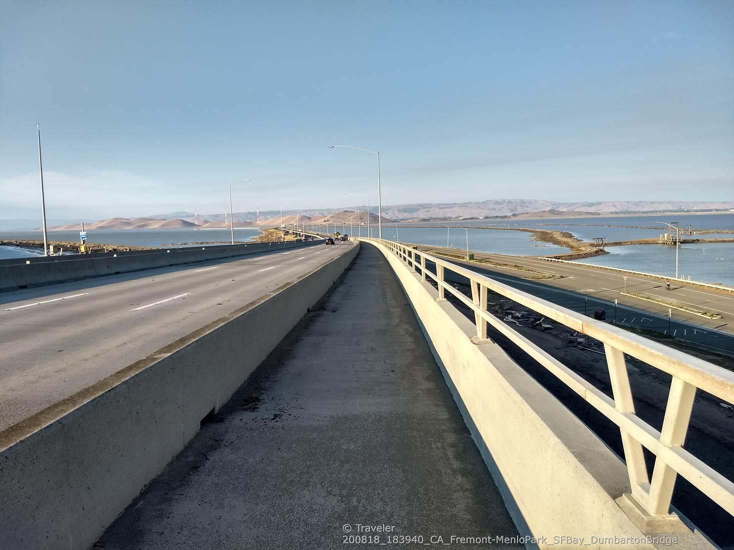 A long concrete bridge over water, with distant mountains under a clear sky.