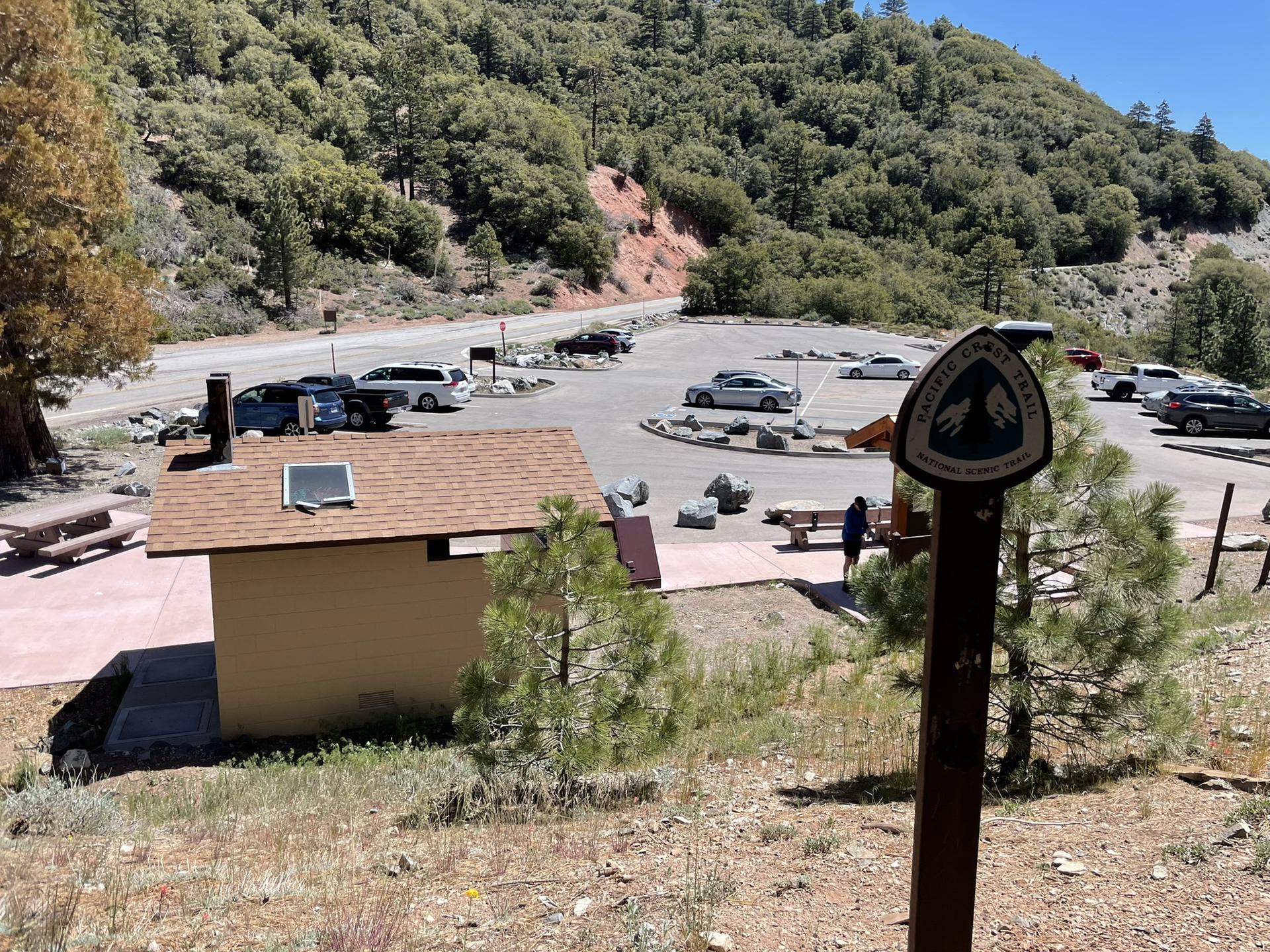 A small building and parking lot with cars, surrounded by mountains.