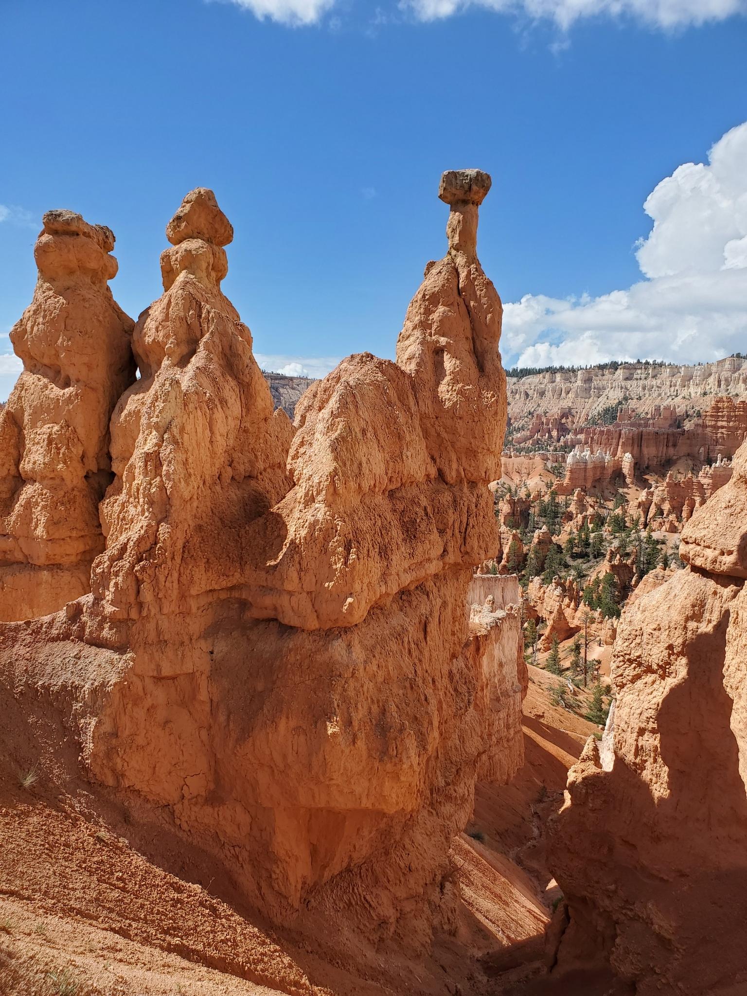 Three prominent orange rock formations against a distant canyon and blue sky.