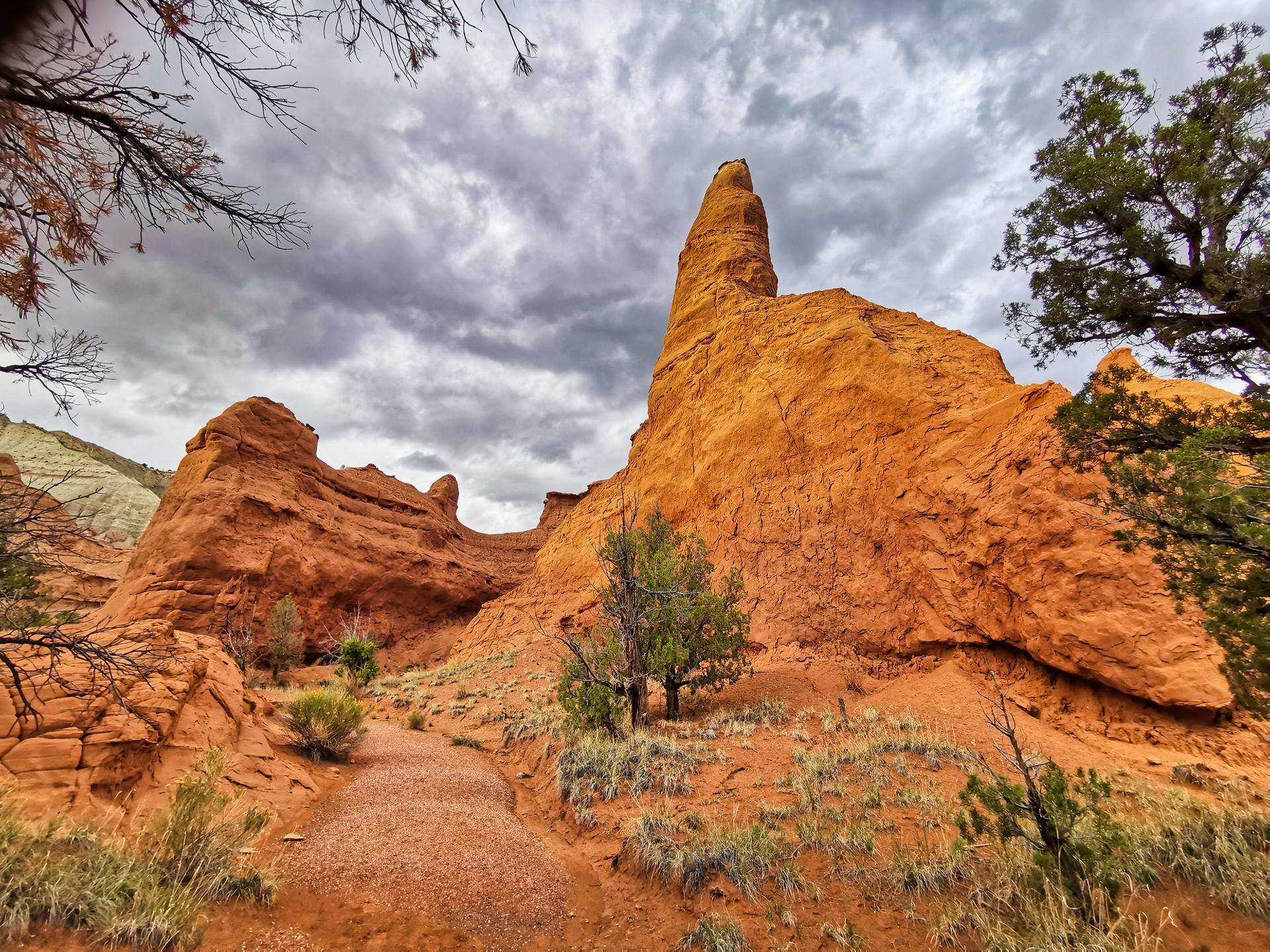 Red rock formation with a pointed peak and a dirt path under a cloudy sky.