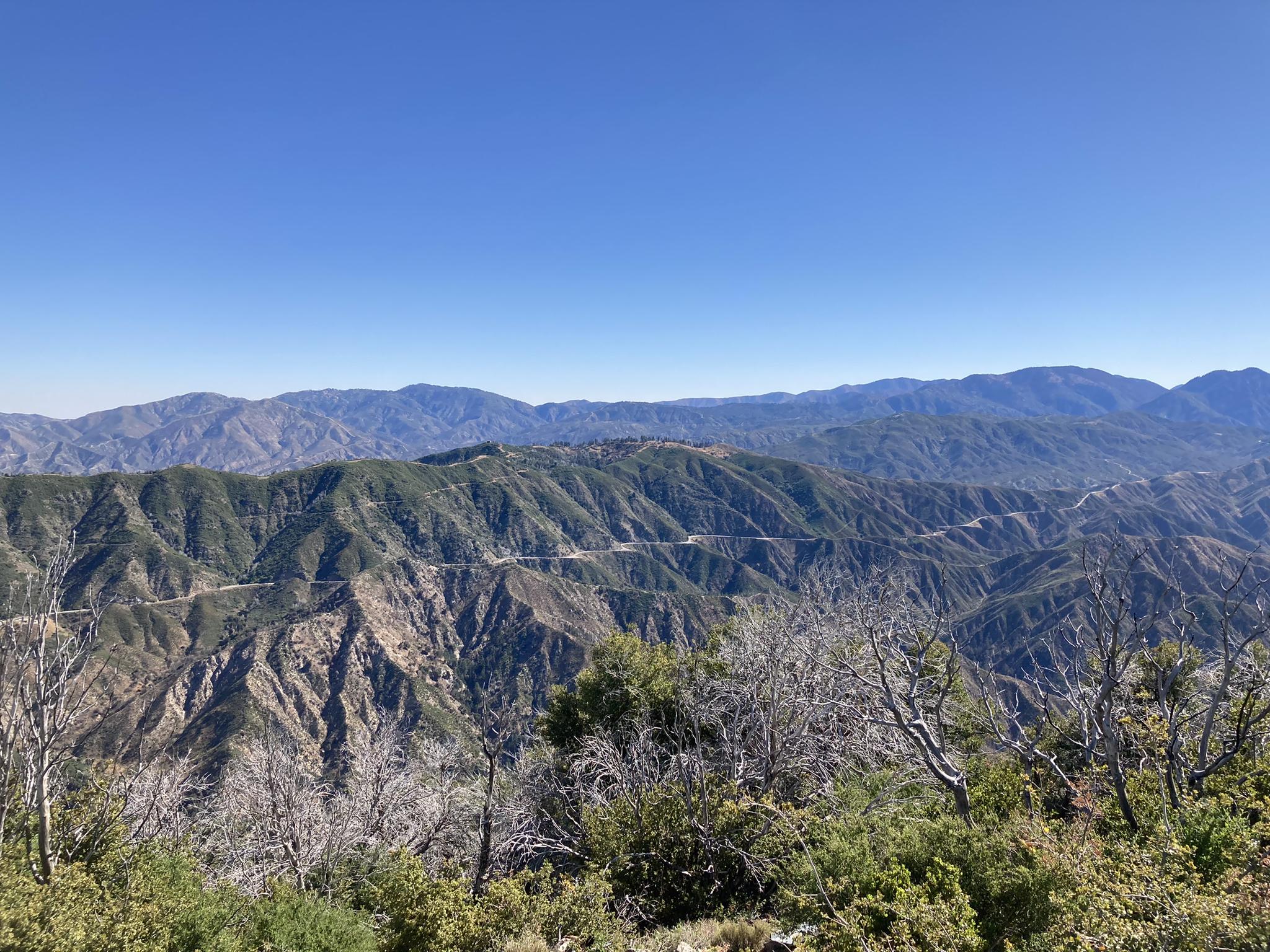 Expansive view of green, rugged mountains with a winding road under a clear sky.