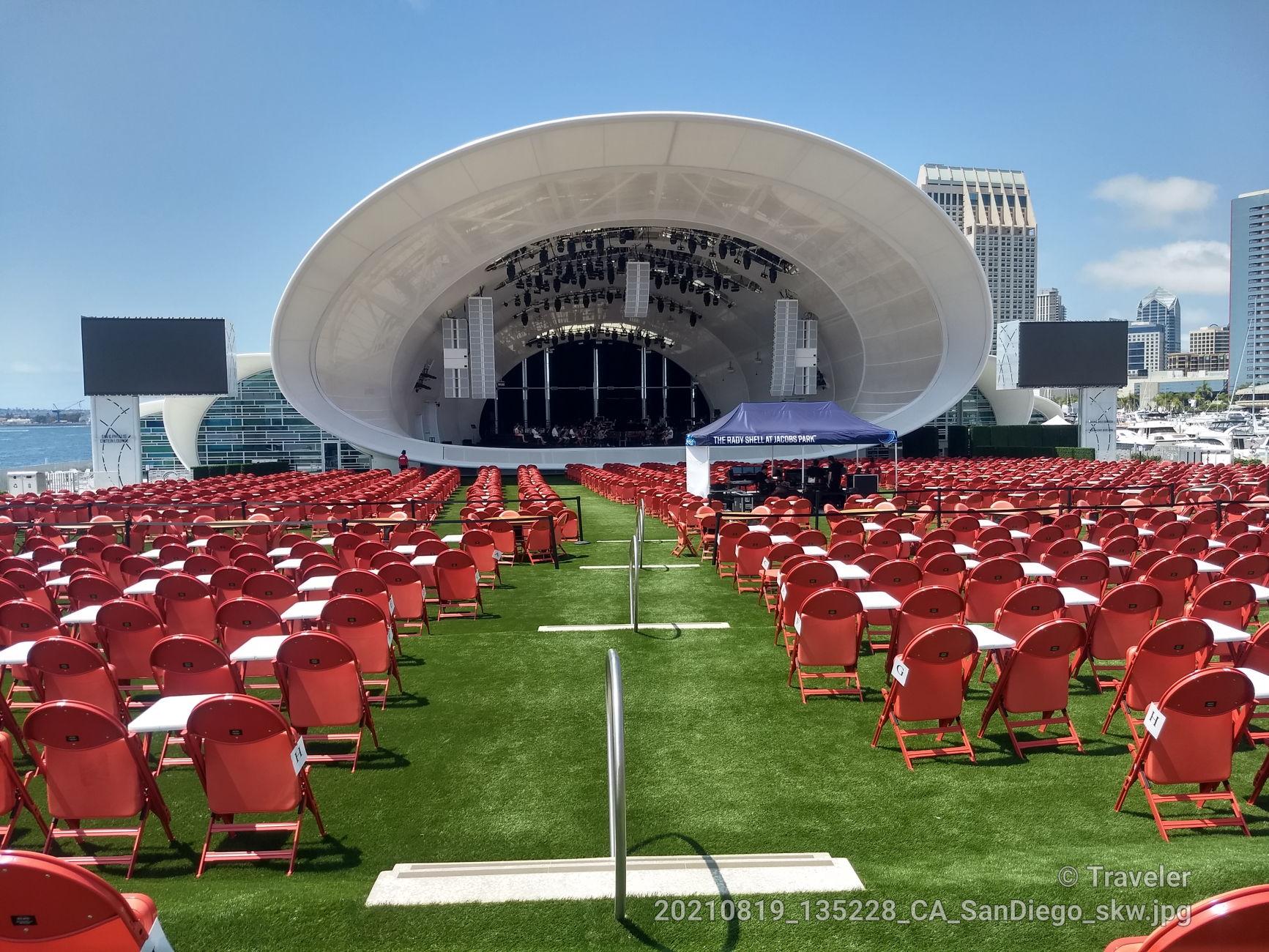 An outdoor concert venue with rows of red chairs facing a large stage.