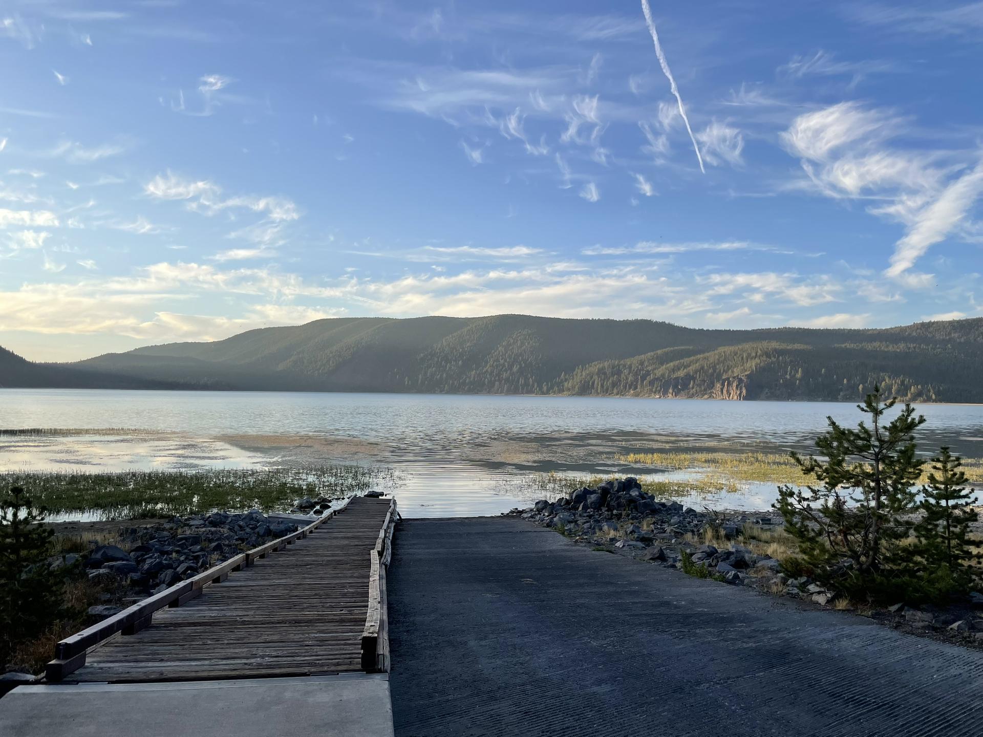 Wooden dock and paved ramp leading to a calm lake with distant hills at sunset.