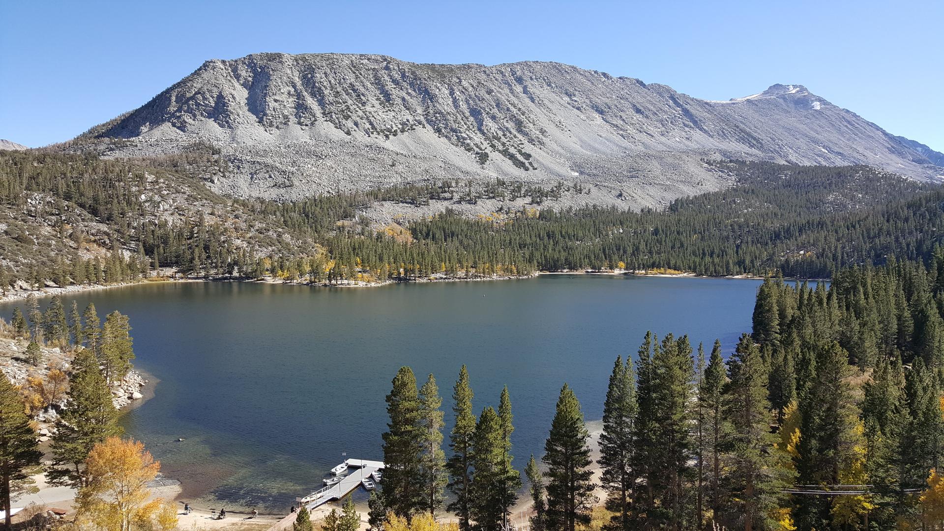 Panoramic view of a large lake surrounded by forest and mountains.
