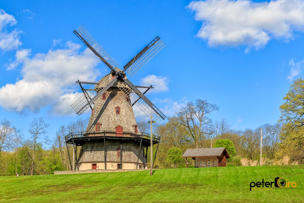 Historic windmill on a vibrant green hill under a bright blue sky.