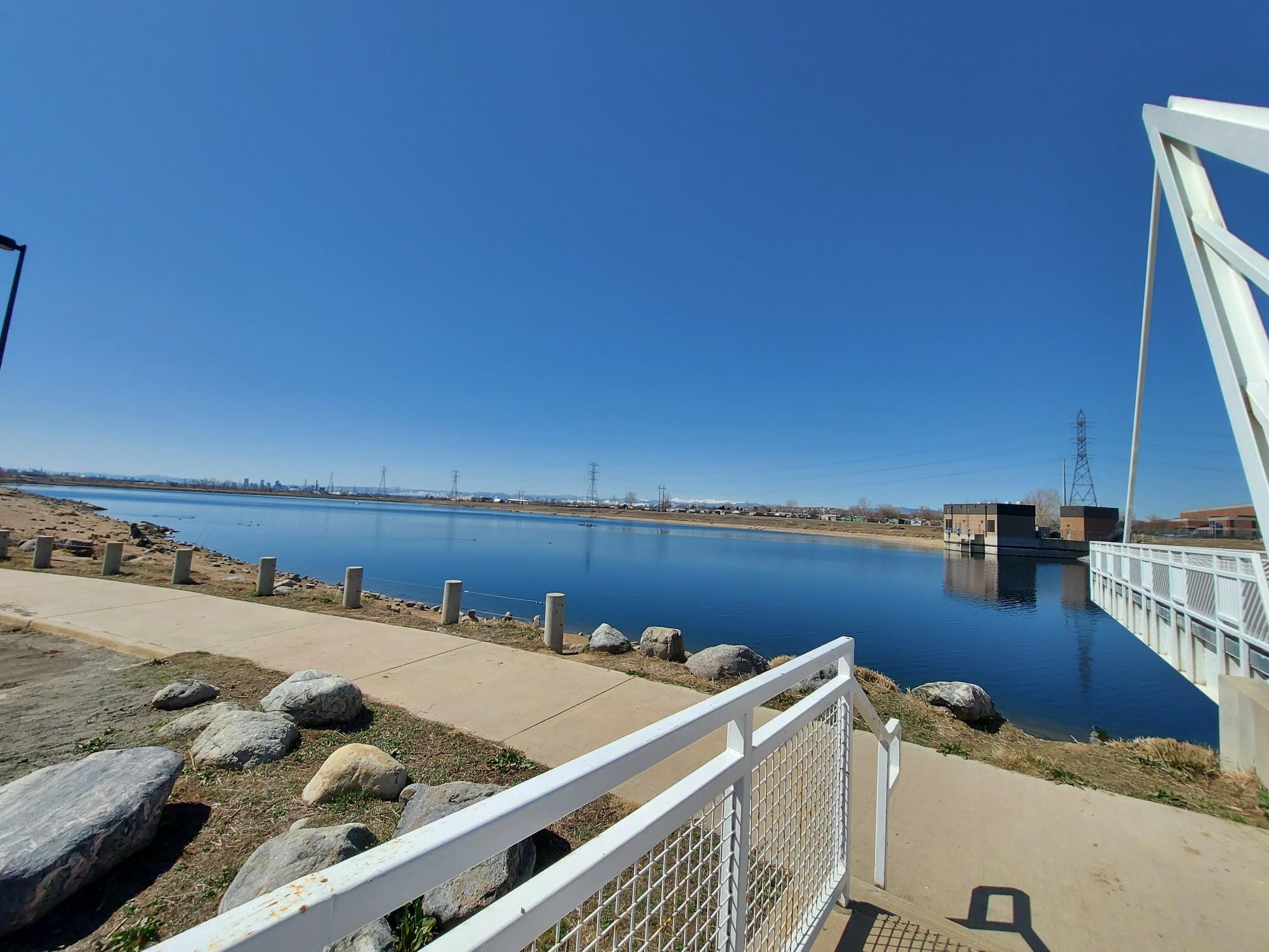 Wide lake next to a paved path and modern white bridge.