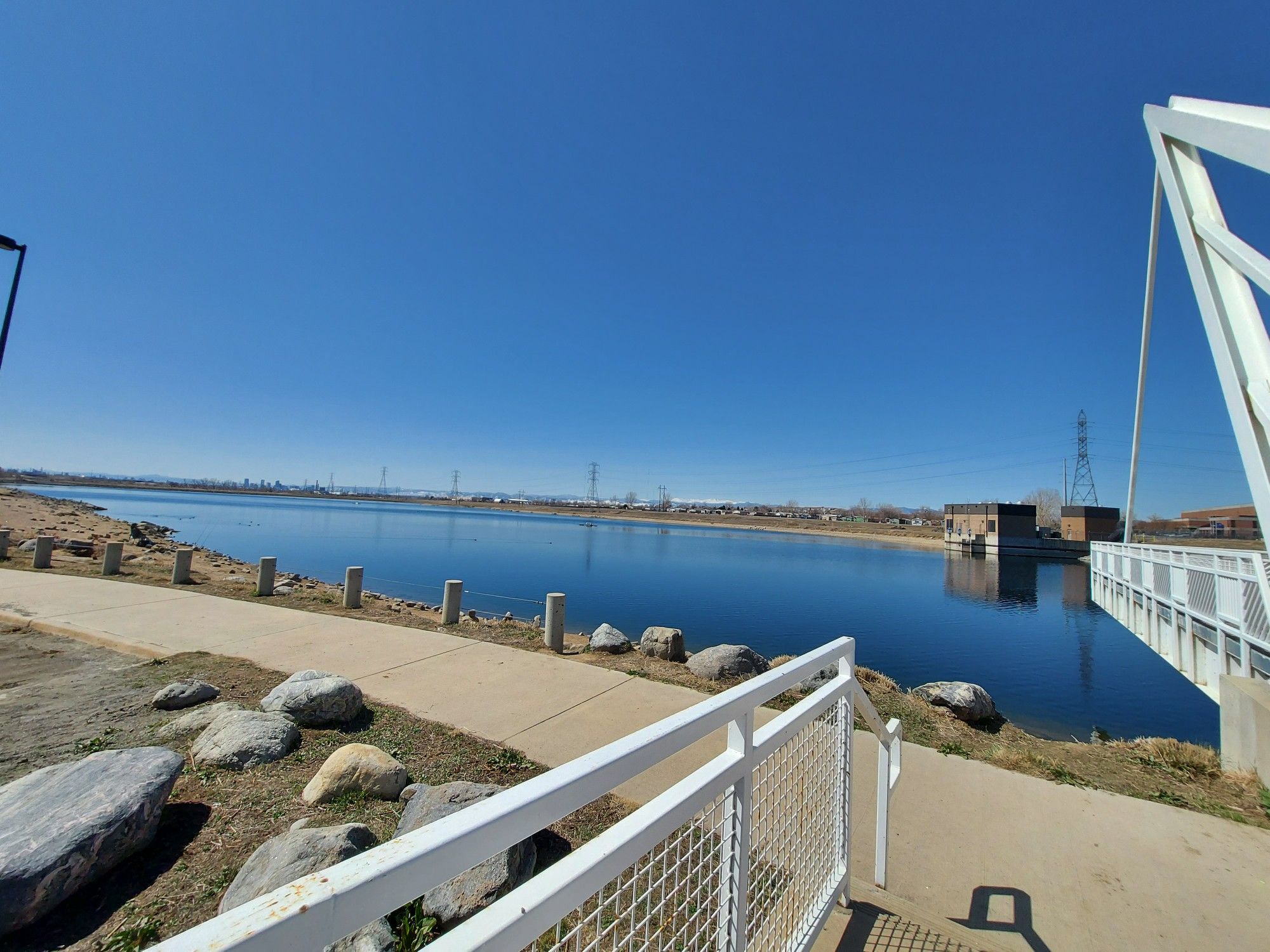 Wide lake next to a paved path and modern white bridge. - South Platte River Trail Loop