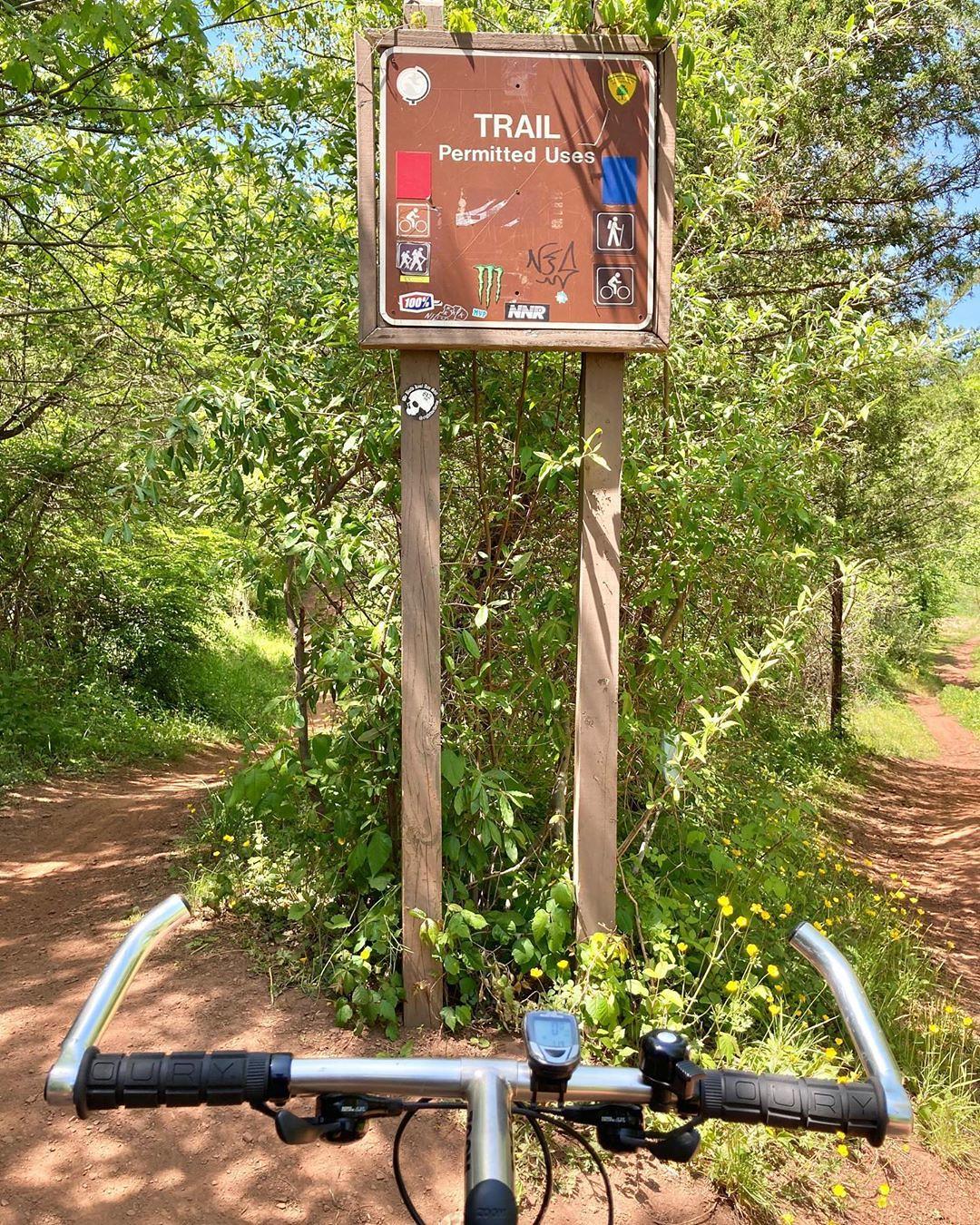 A trail sign with permitted uses, viewed from a bicycle's handlebars.