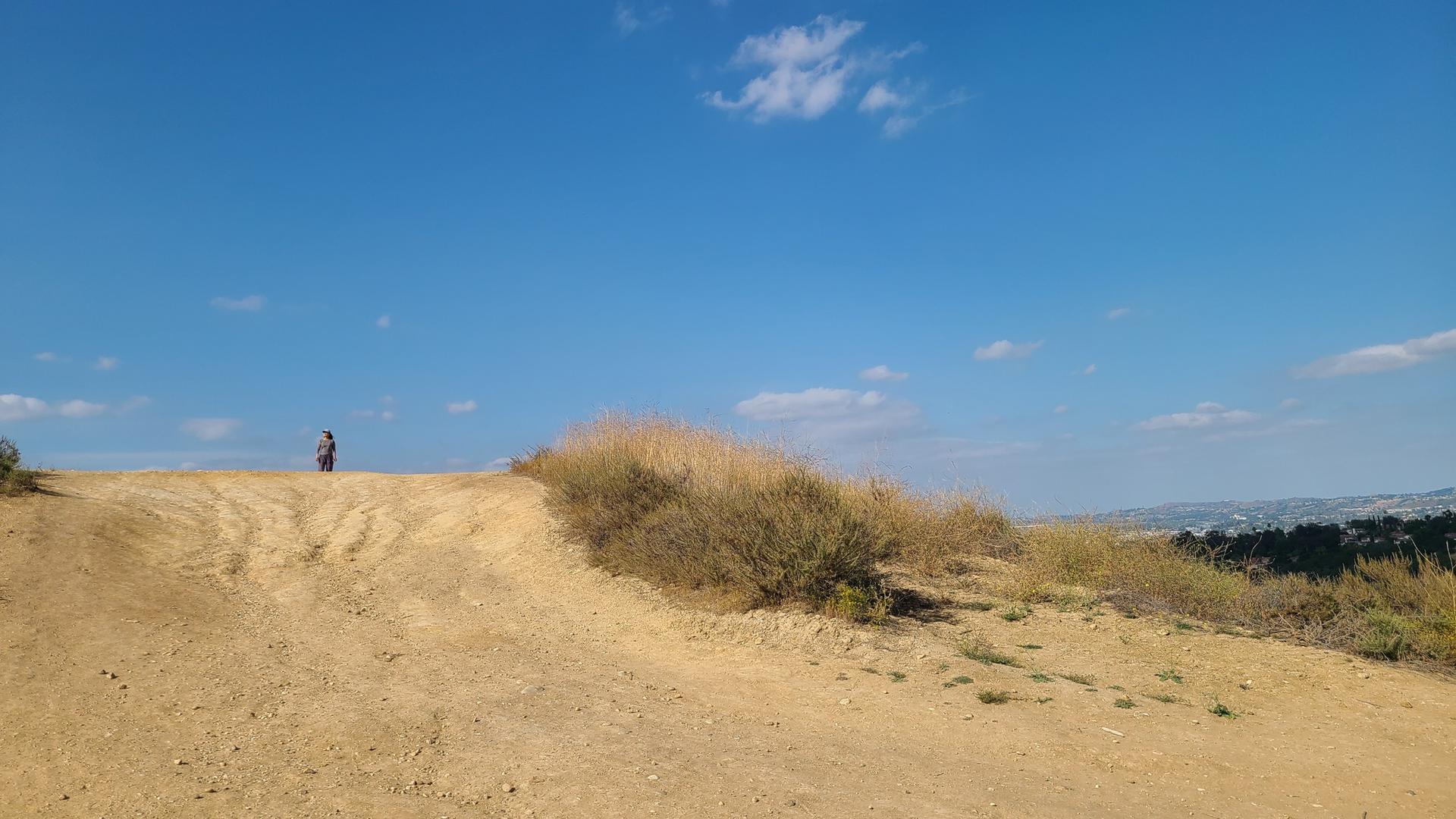 A person stands on a dusty hill under a bright blue sky.