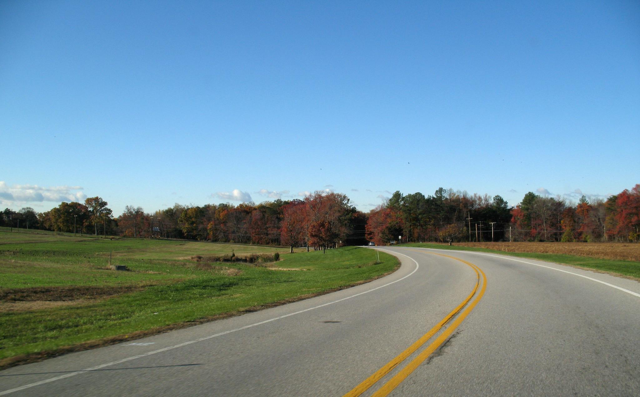 A winding road through autumn fields and colorful trees under a clear blue sky.