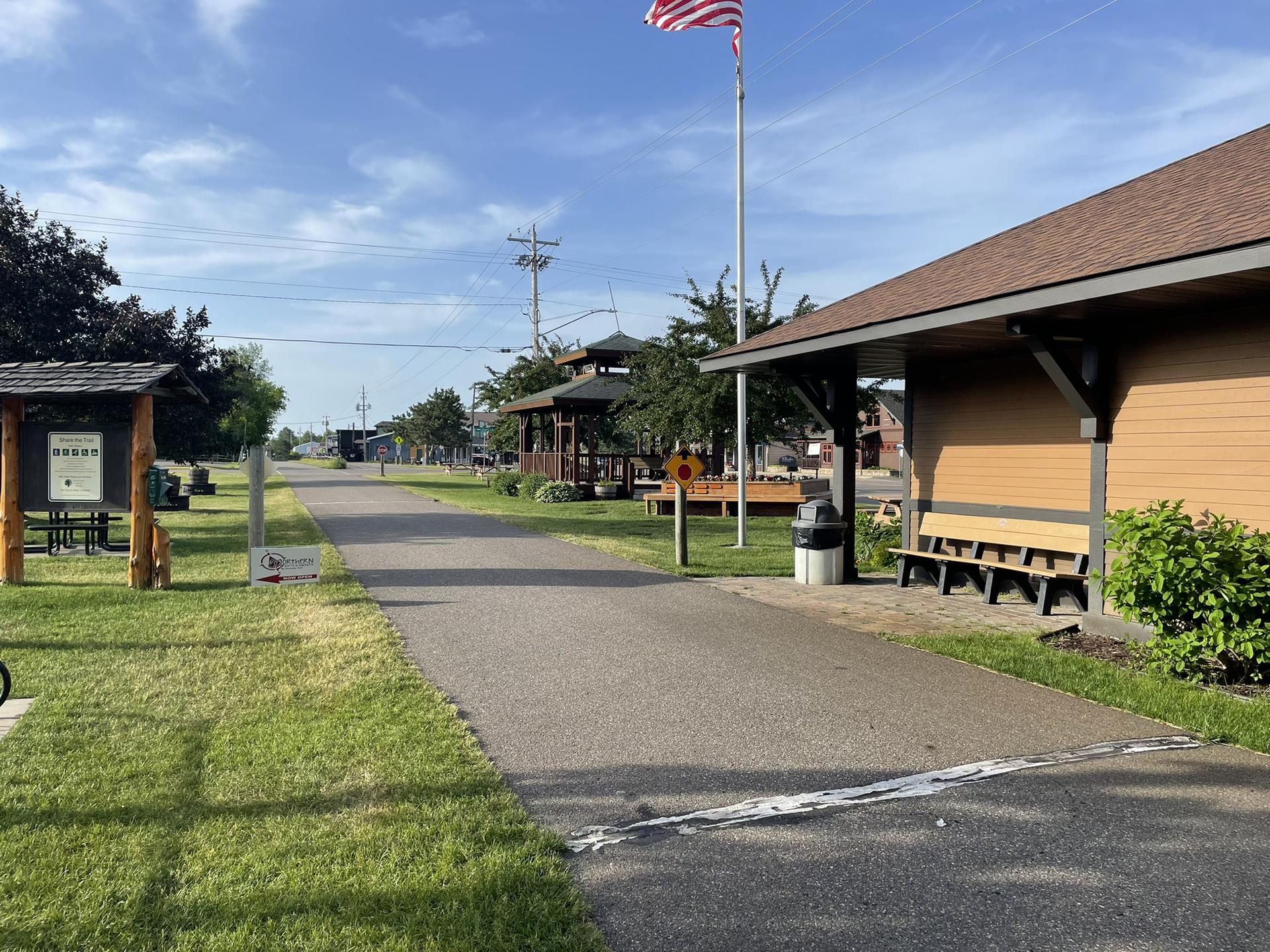 Paved path leading to a building with a flag, benches, and a gazebo.