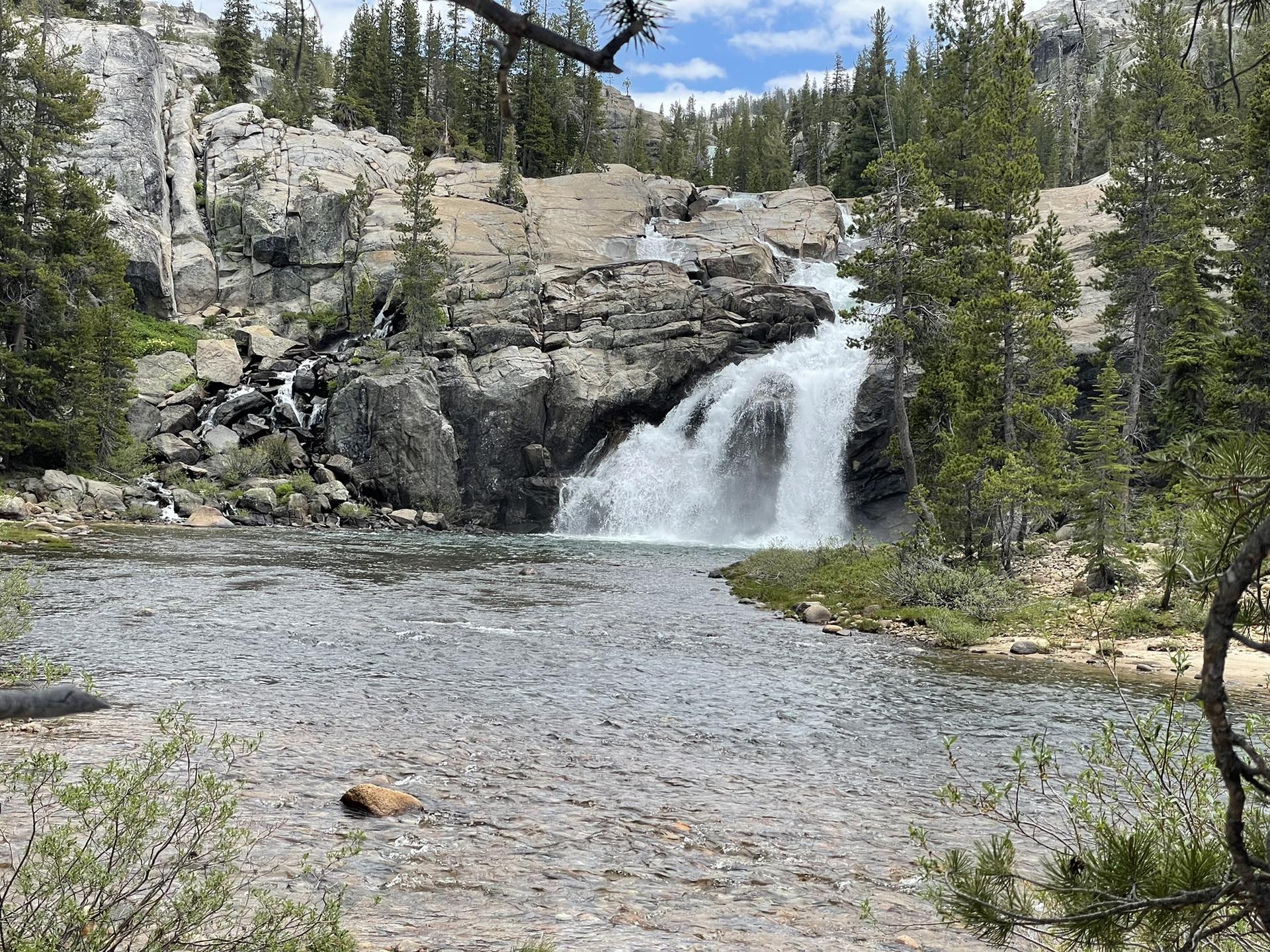 A powerful waterfall cascades into a river surrounded by rocky cliffs and trees.