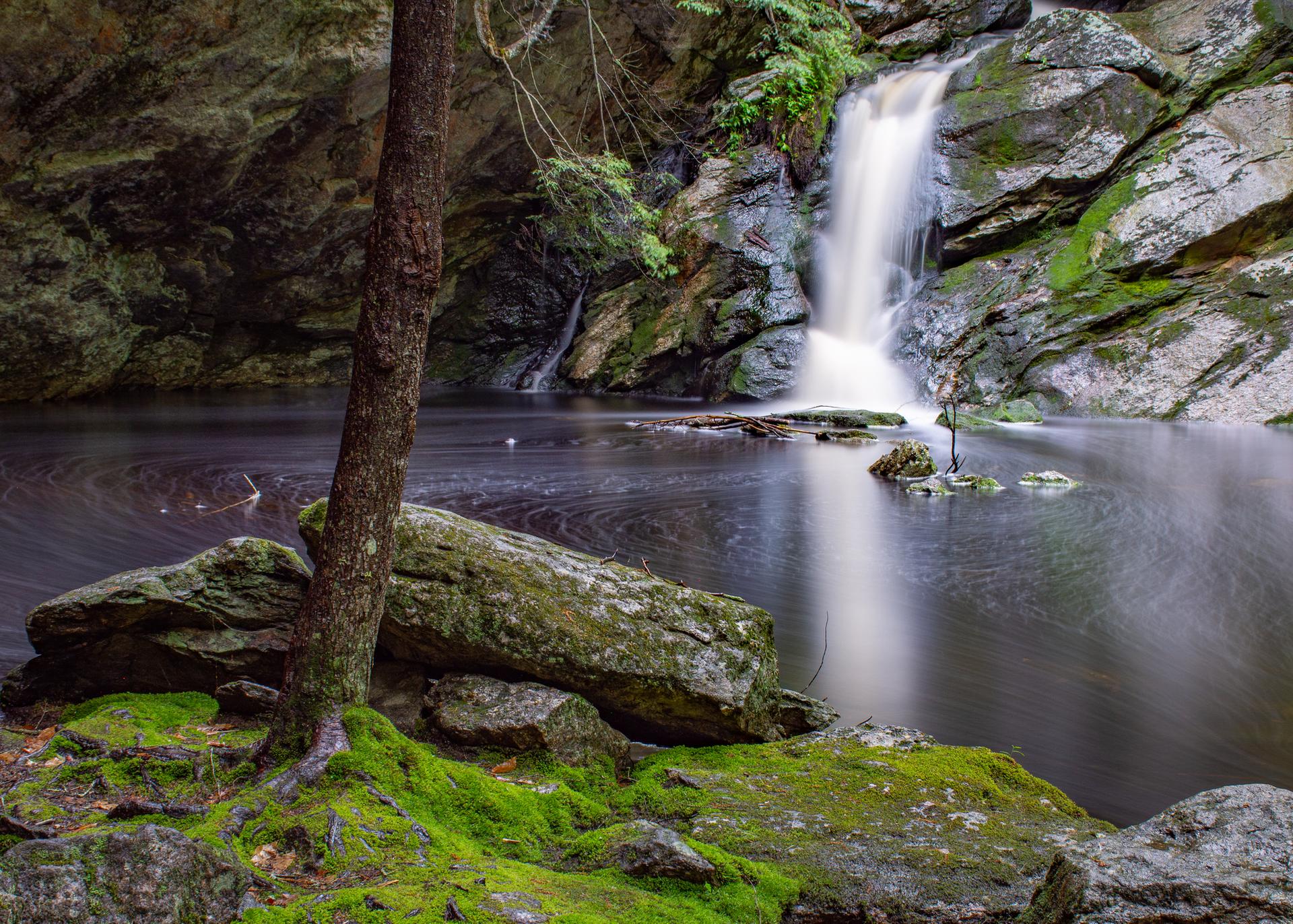 A long-exposure waterfall cascades into a dark pool surrounded by mossy rocks.