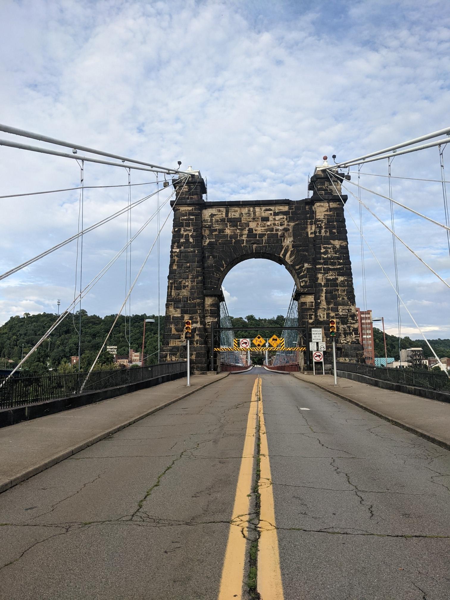A historic stone bridge arch frames a road under a cloudy sky.