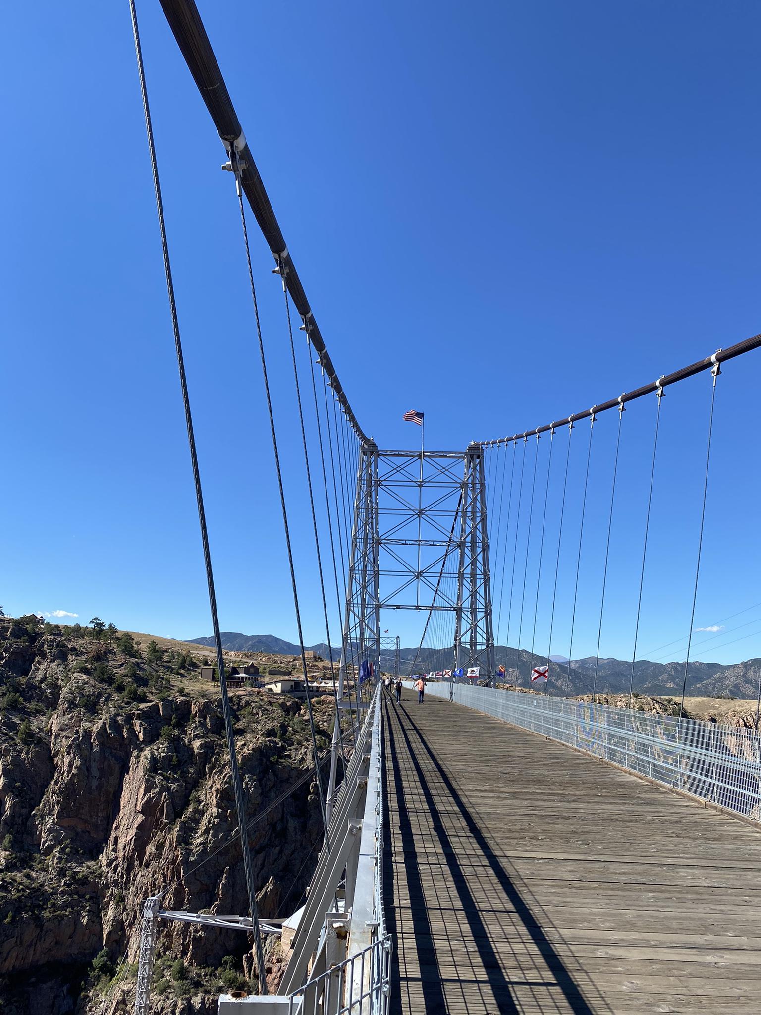 Long suspension bridge stretching over a canyon under a clear blue sky.