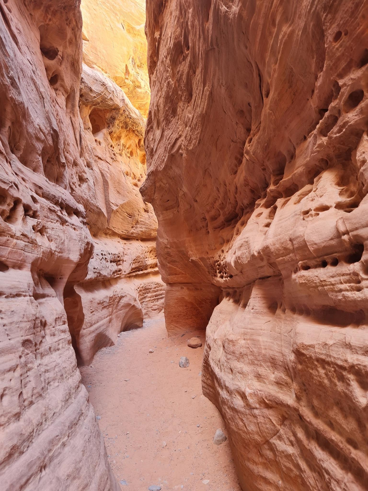 Deep, narrow slot canyon with textured orange rock walls and sandy floor.