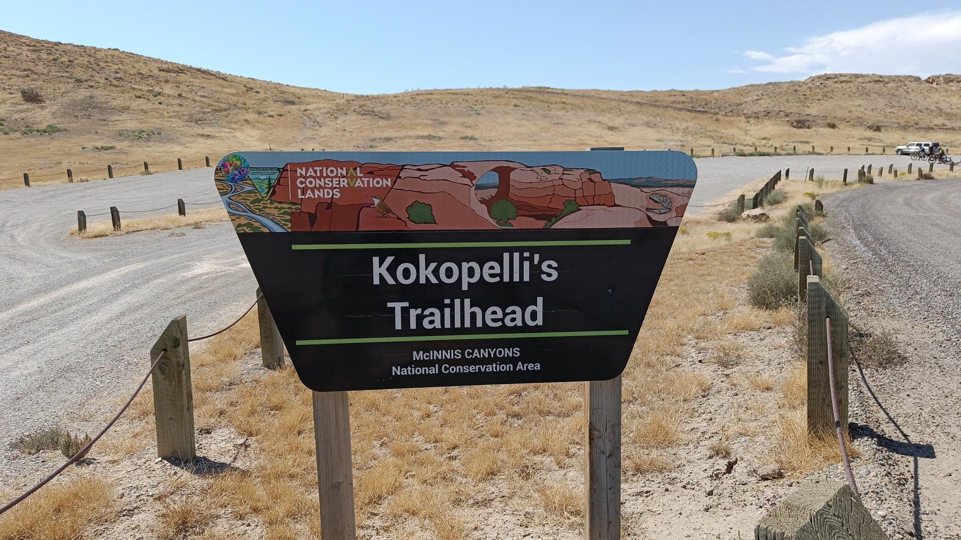 A trailhead sign in a dry, open landscape under a clear sky.