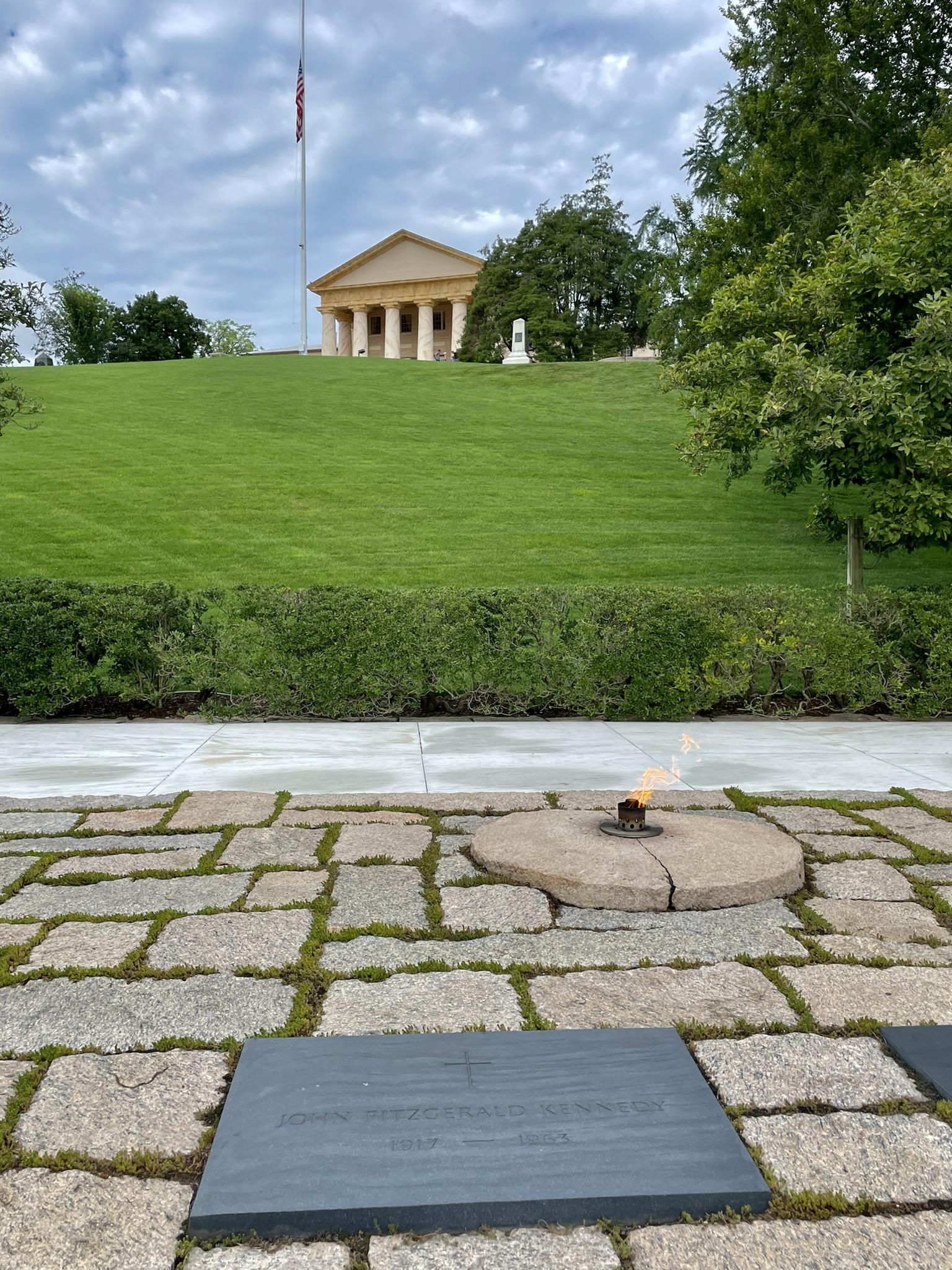 Eternal flame and grave markers in foreground, classical building on a green hill.