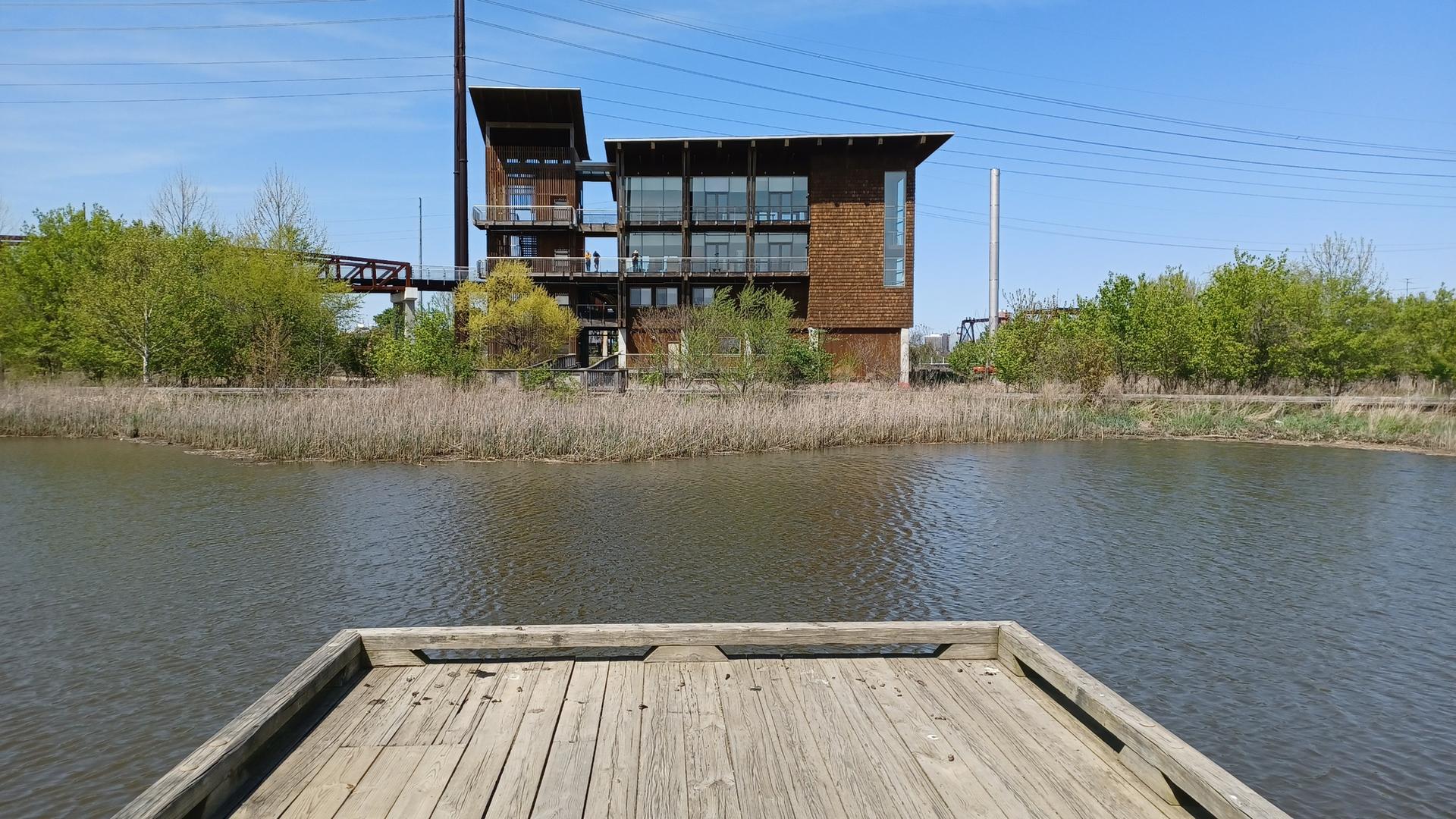 A wooden dock extends into a river, with an industrial building in the background.