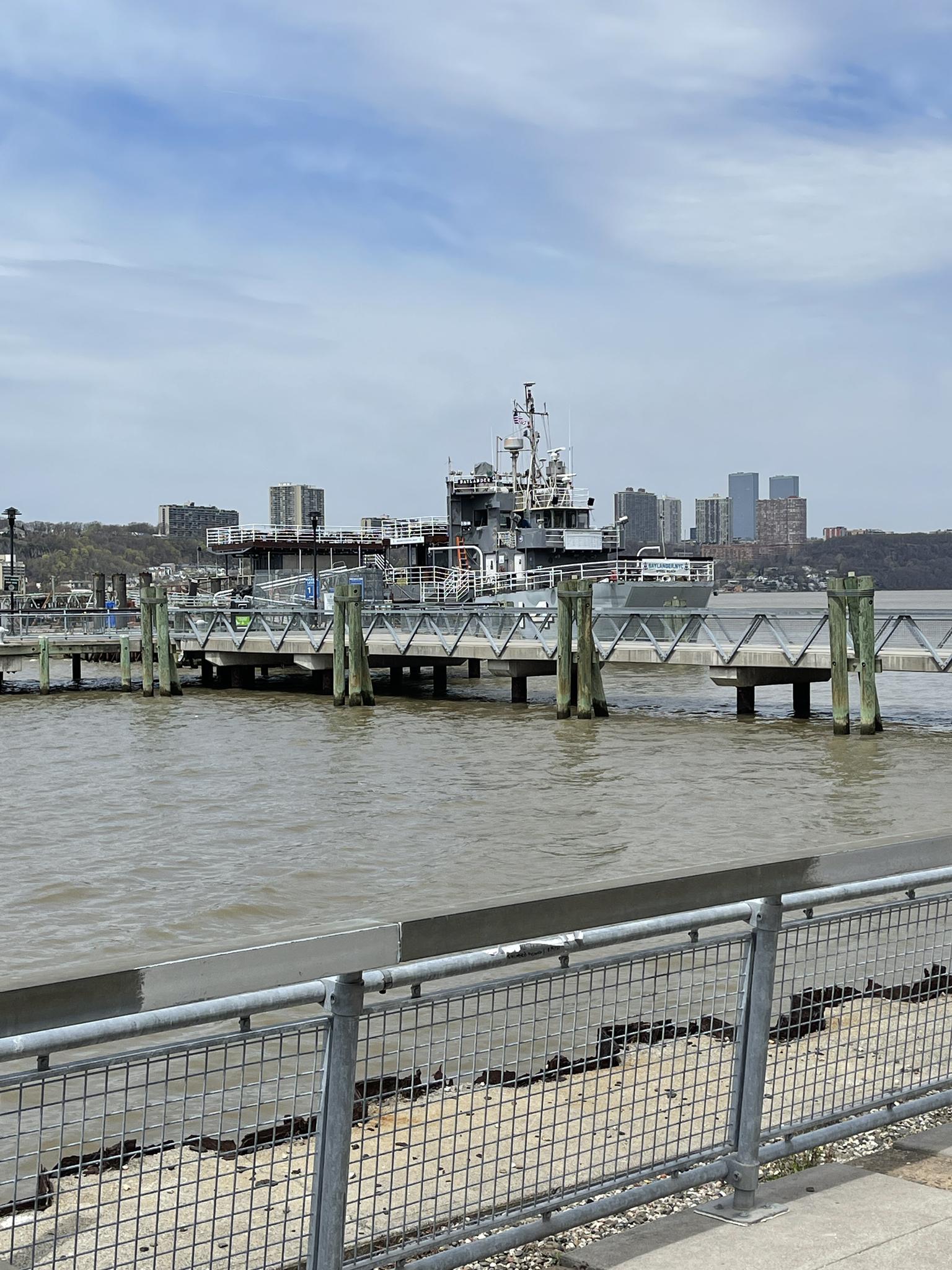 A large ship docked at a pier on a wide river under a cloudy sky.