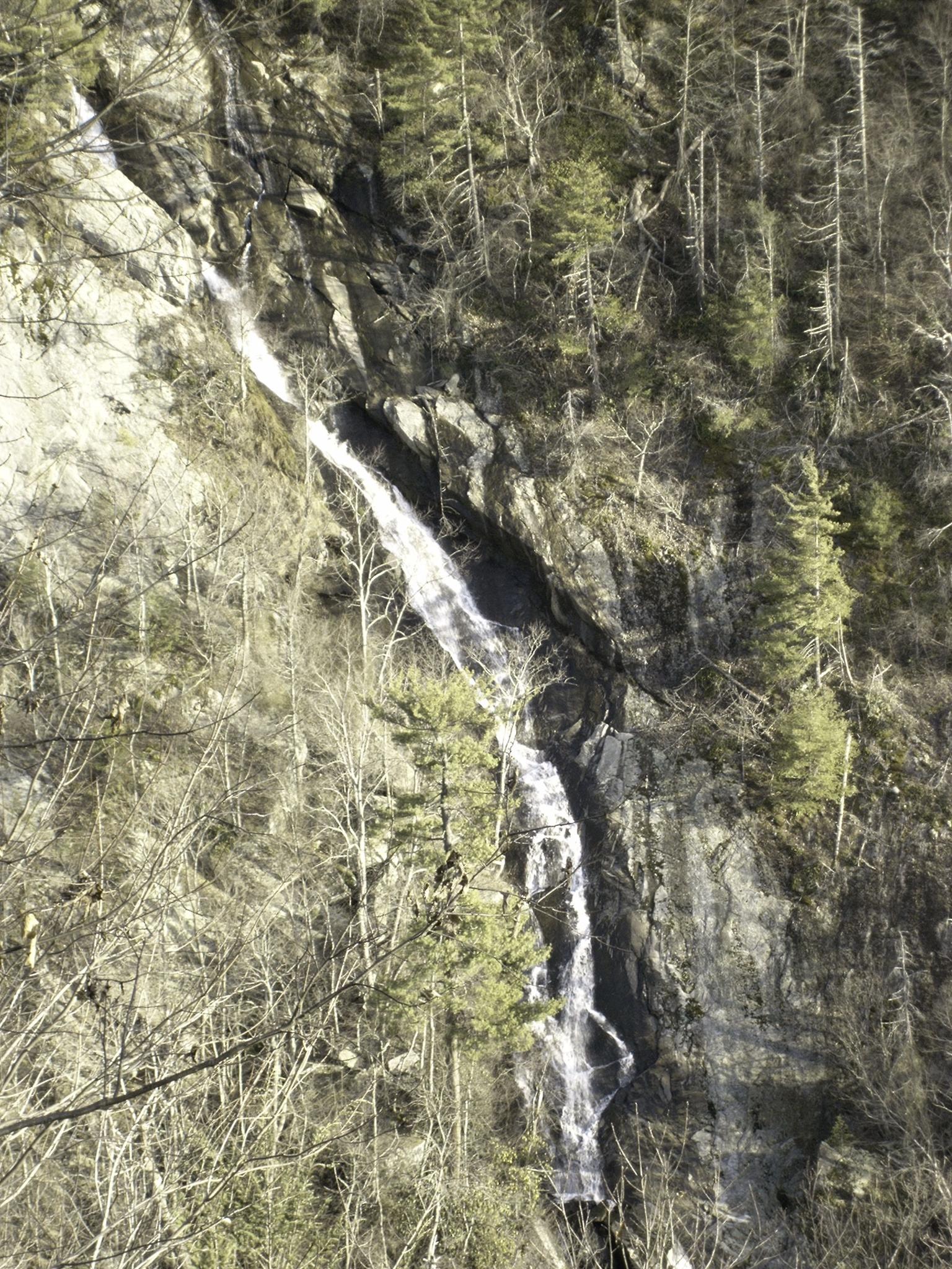 A tall, narrow waterfall cascades down a rocky cliff with bare trees.