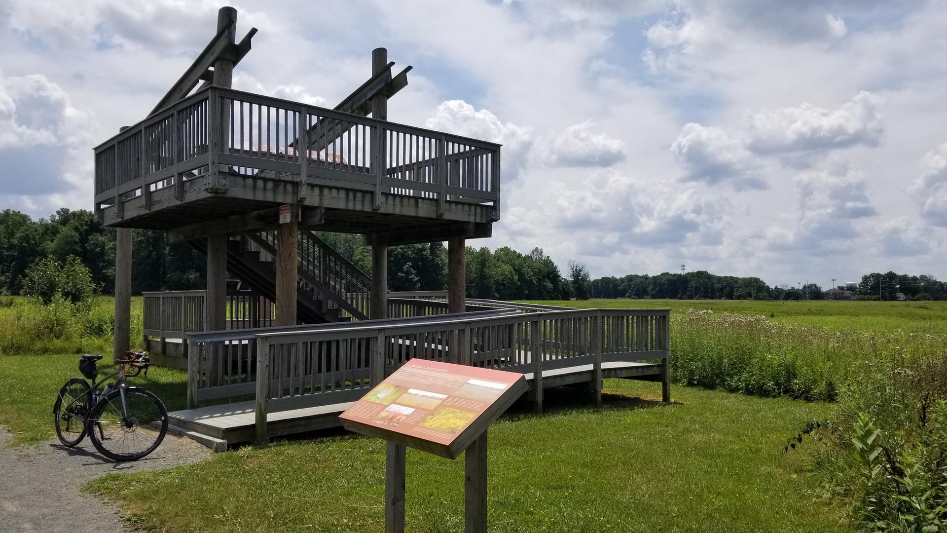 Two-story wooden observation deck and bicycle in a sunny, grassy field.