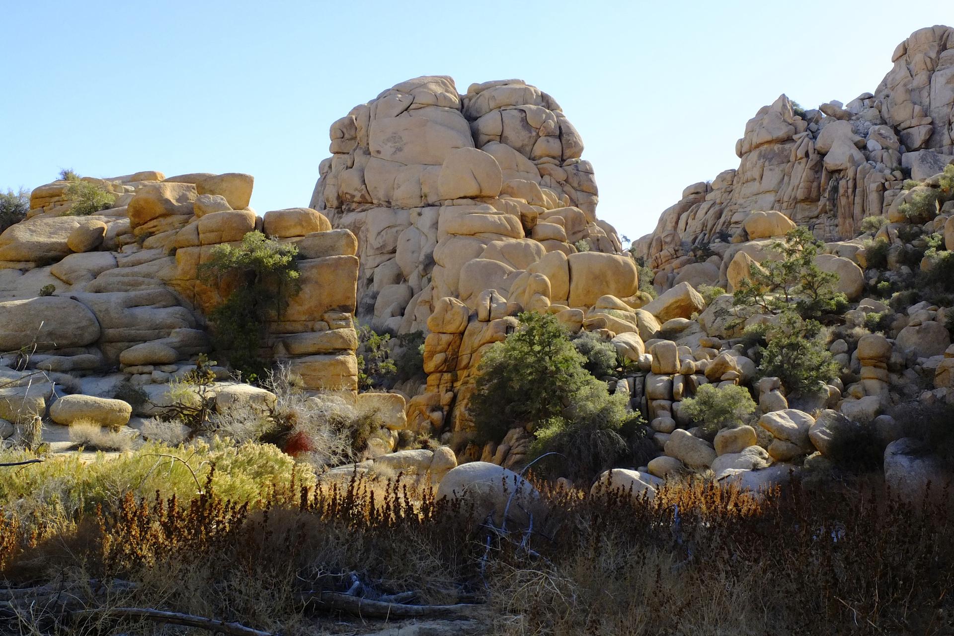 Towering, stacked rock formations in a sunny desert landscape with dry brush.