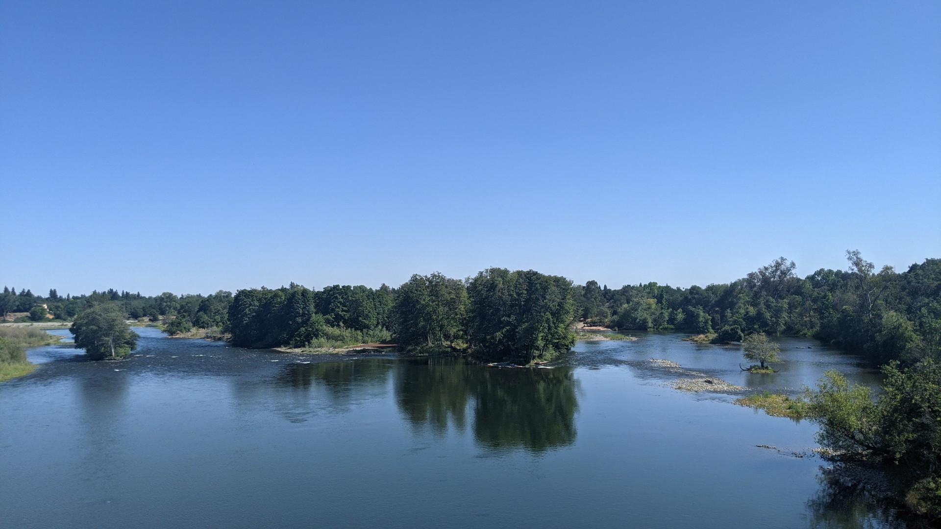 Wide river with tree-covered islands under a clear blue sky.