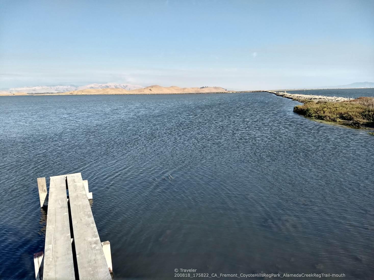 A wooden pier extends into a wide, calm water body on a clear day.