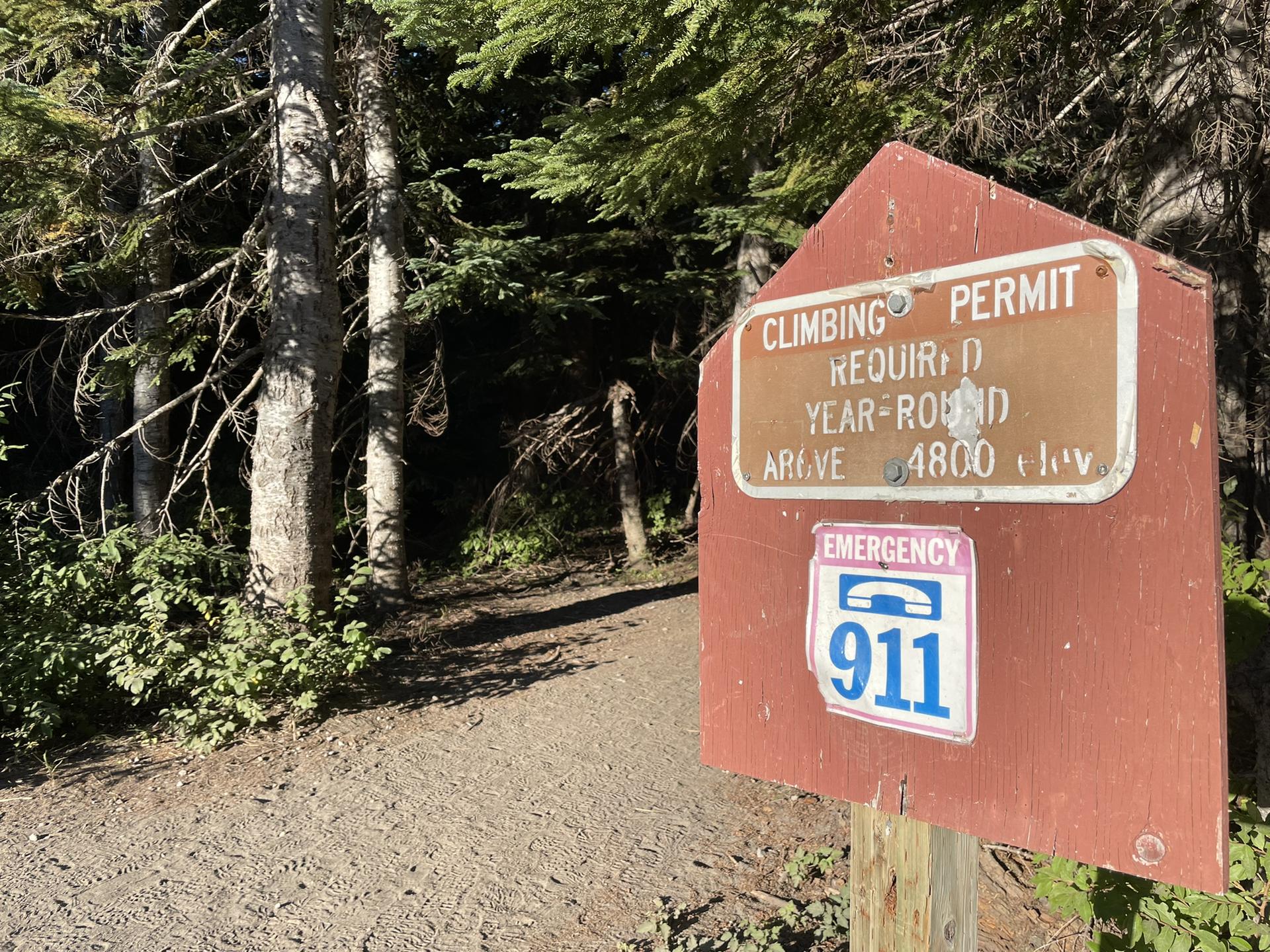 Wooden sign on a forest trail, 'Climbing Permit Required' text visible.