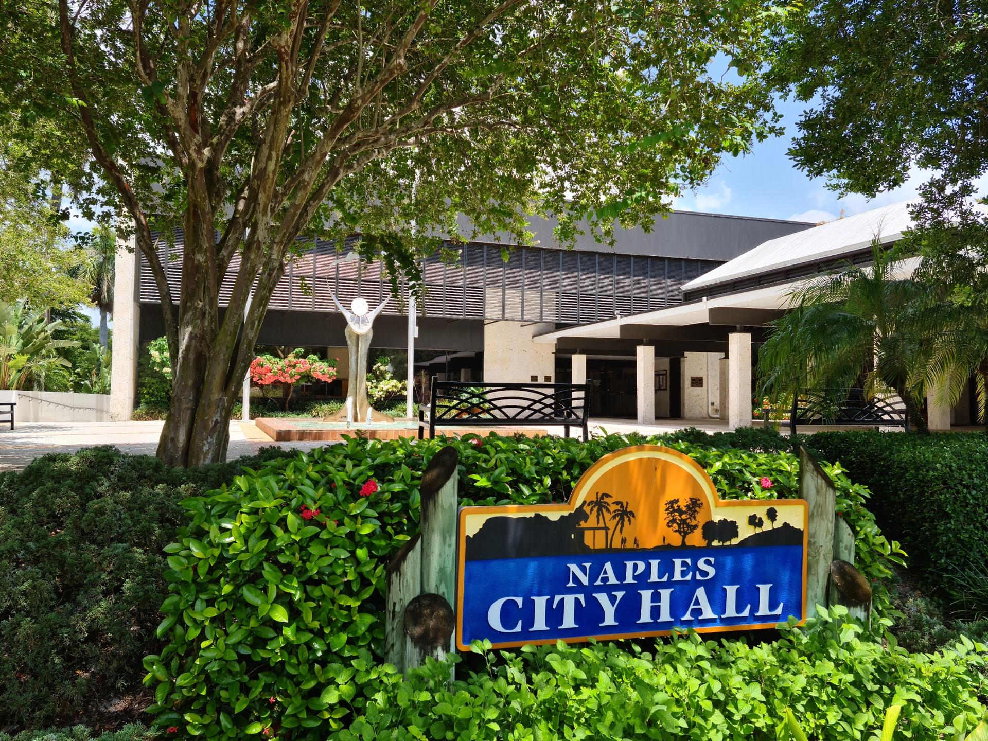 A "City Hall" sign surrounded by green landscaping and a building.