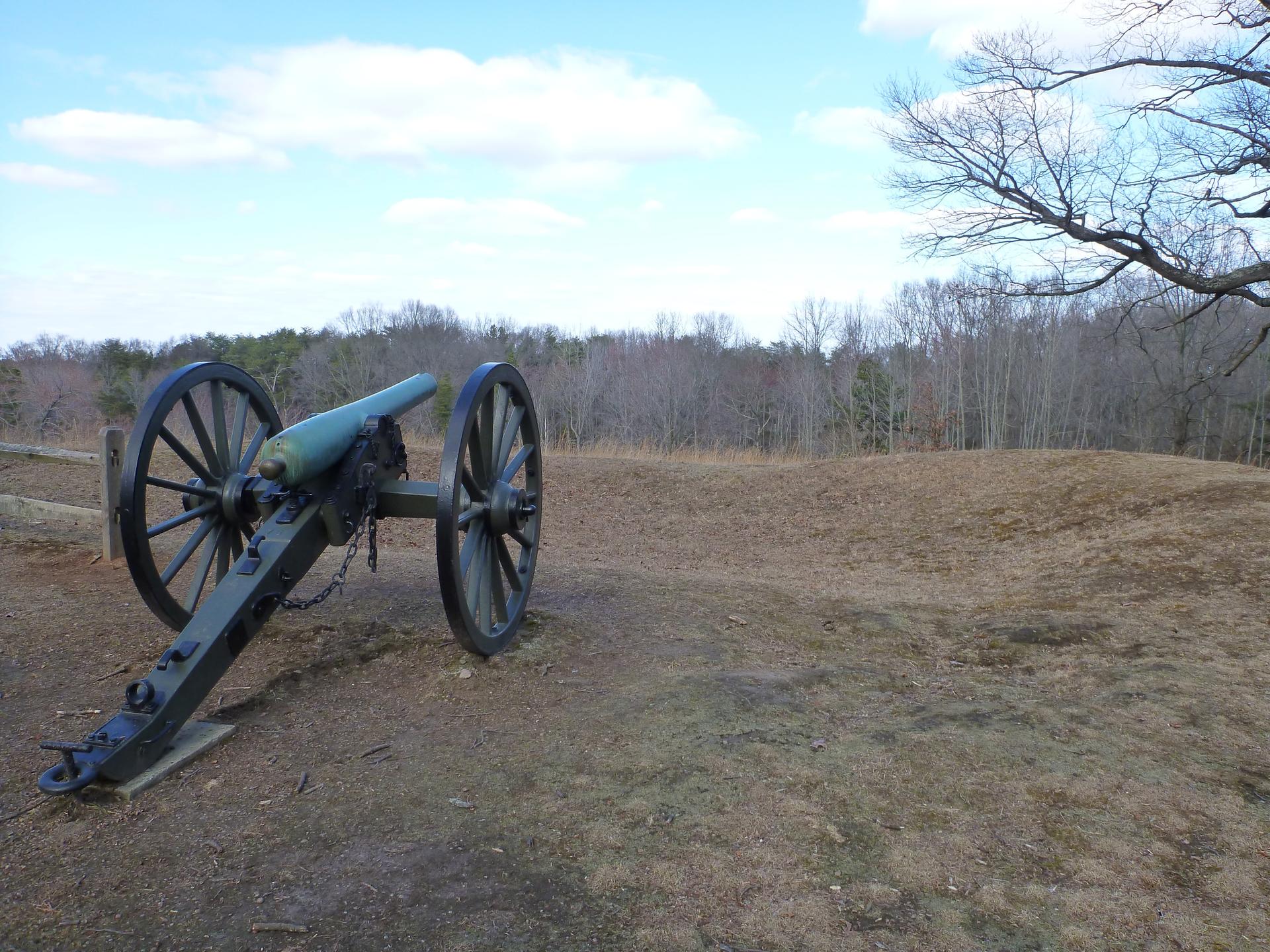 An old cannon on a grassy hill under a bright sky with bare trees.
