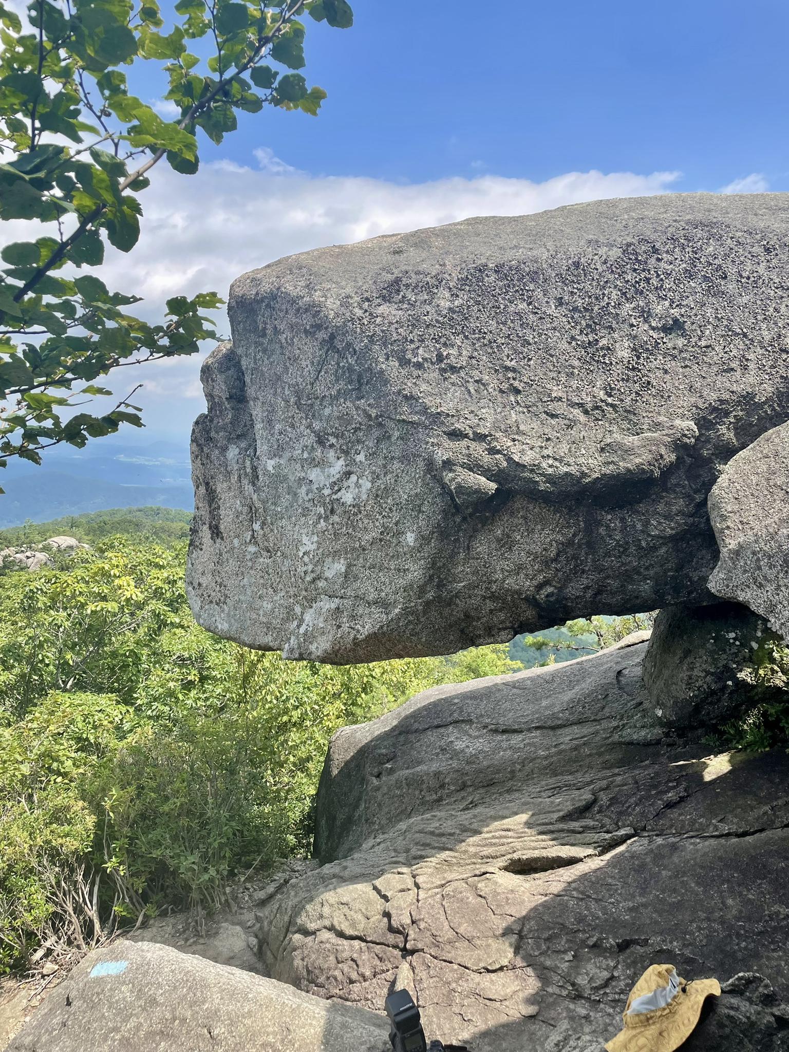 Large overhanging rock formation with green trees and distant mountain views.