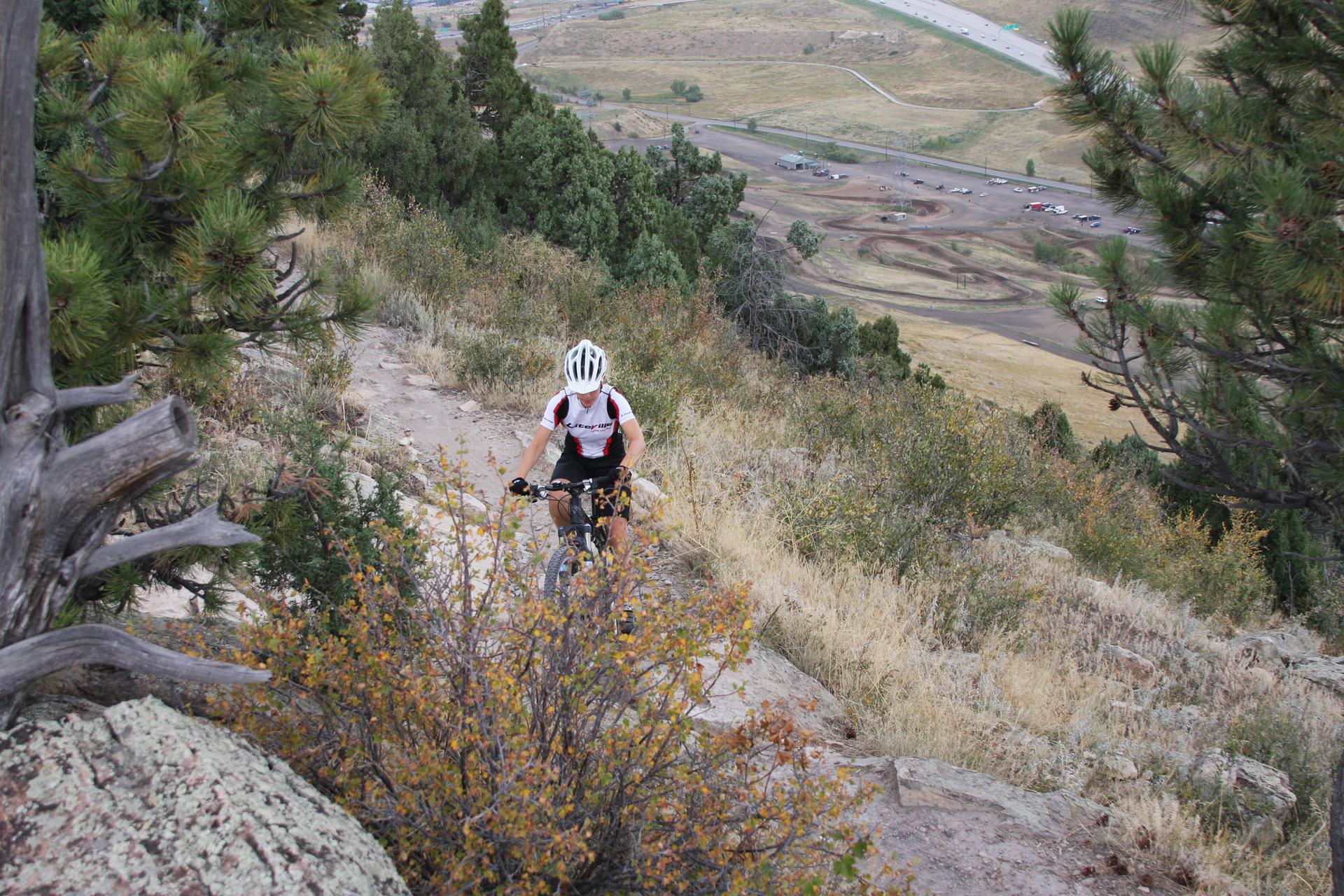 A person mountain biking down a steep, dry, forested hillside on a sunny day.