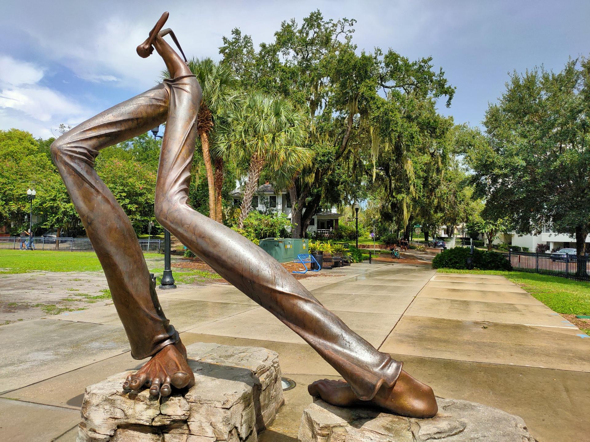 Bronze sculpture of giant legs and feet on a paved path in a park.