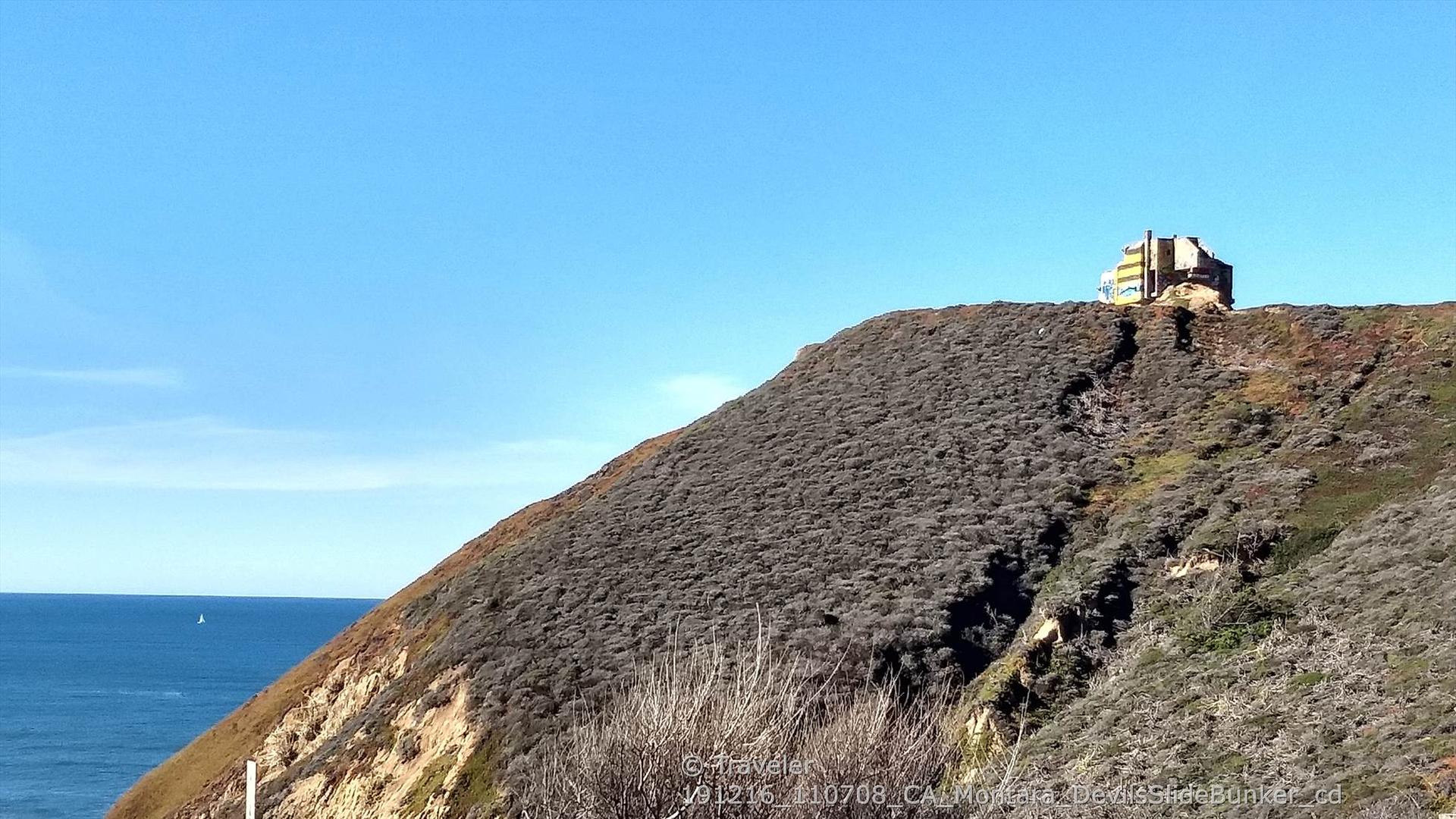 Distant building on a steep, brush-covered hill overlooking the ocean.