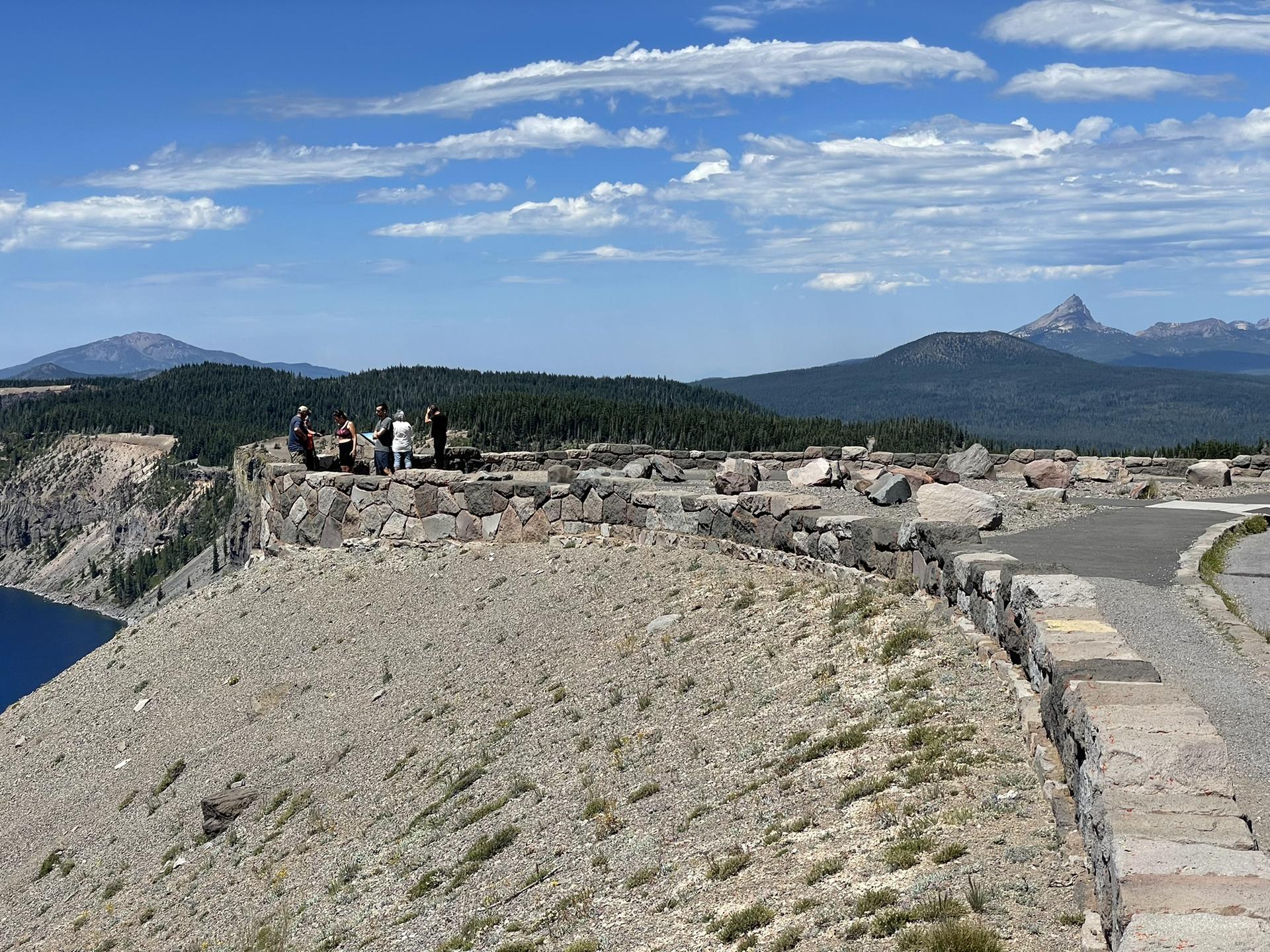 Group of people on a stone viewpoint overlooking a vast valley and mountains.