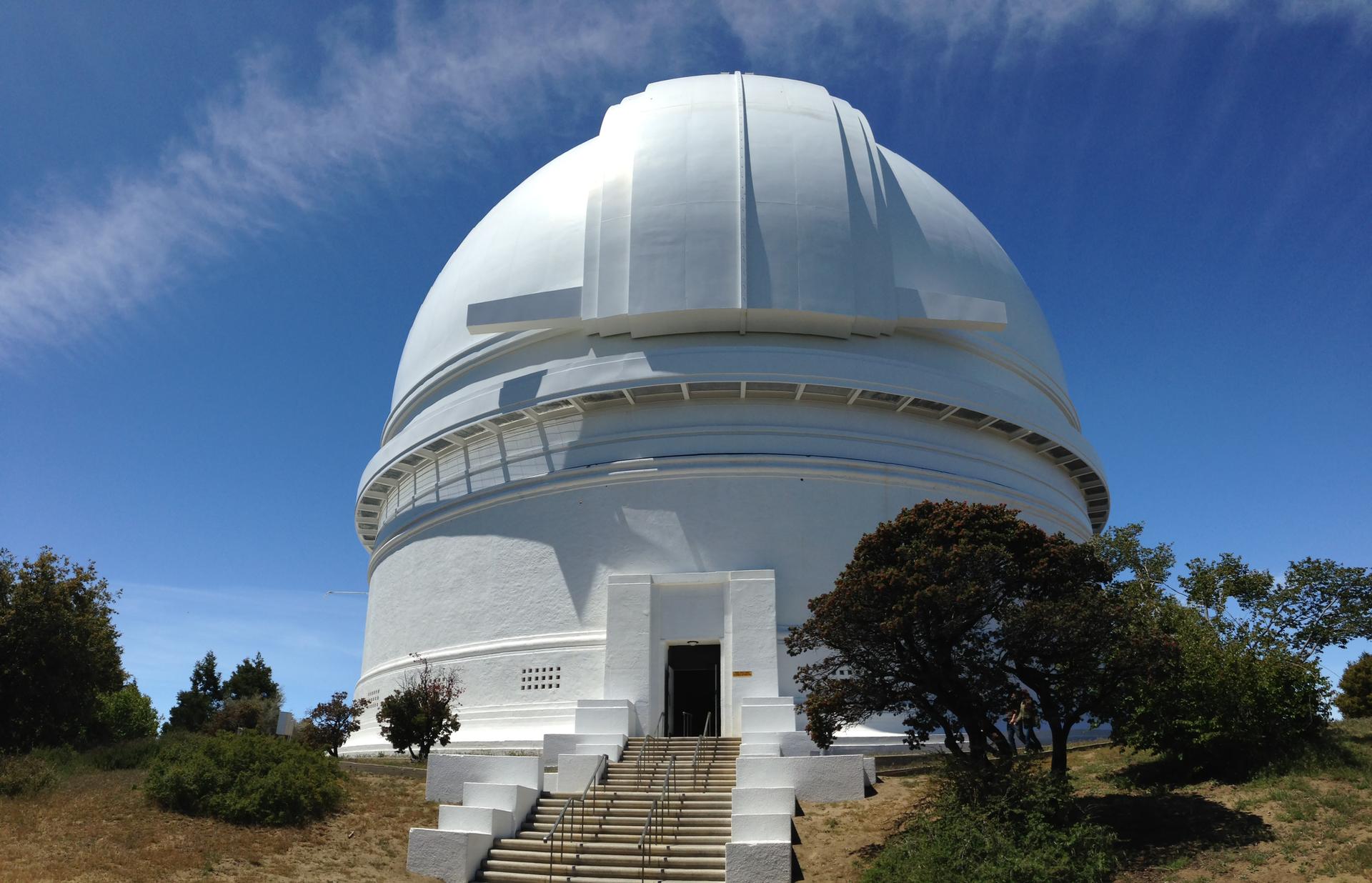 A large white observatory dome stands on a sunny hill.