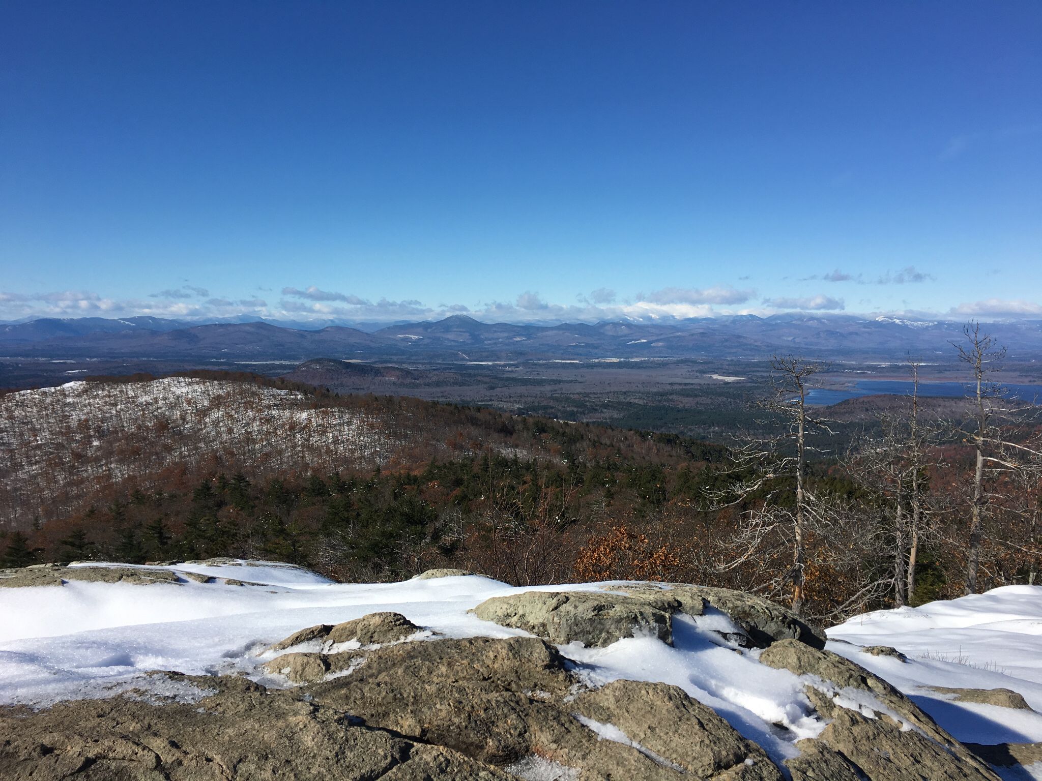 Sunny winter mountain vista with snow-covered rocks and distant peaks under a blue sky. - Ledges Trail