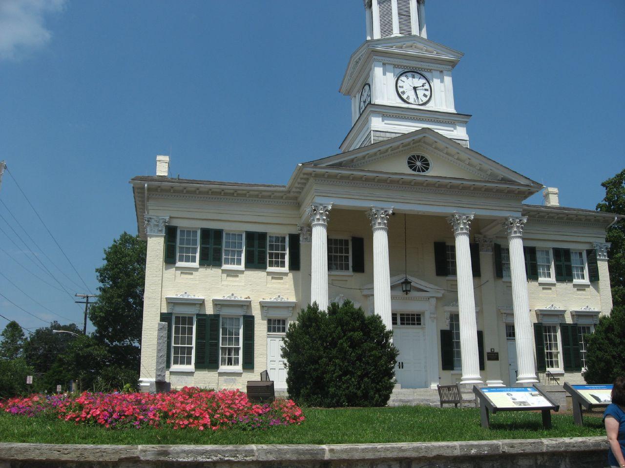 Grand white building with a clock tower, columns, and red flowers.