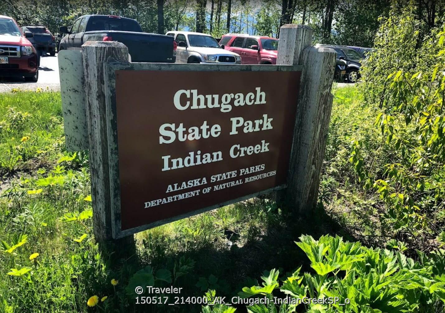 A brown wooden sign in a grassy area with parked cars.